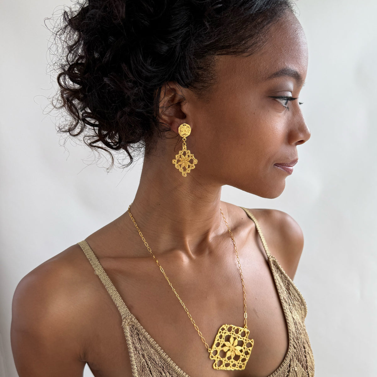 Model wearing chandelier lace earrings and lace pendant necklace, both in 24k gold.
