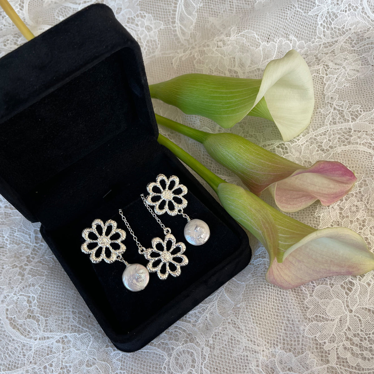 Pair of silver floral lace earrings with baroque coin pearls and floral necklace in a black suede jewelry box.