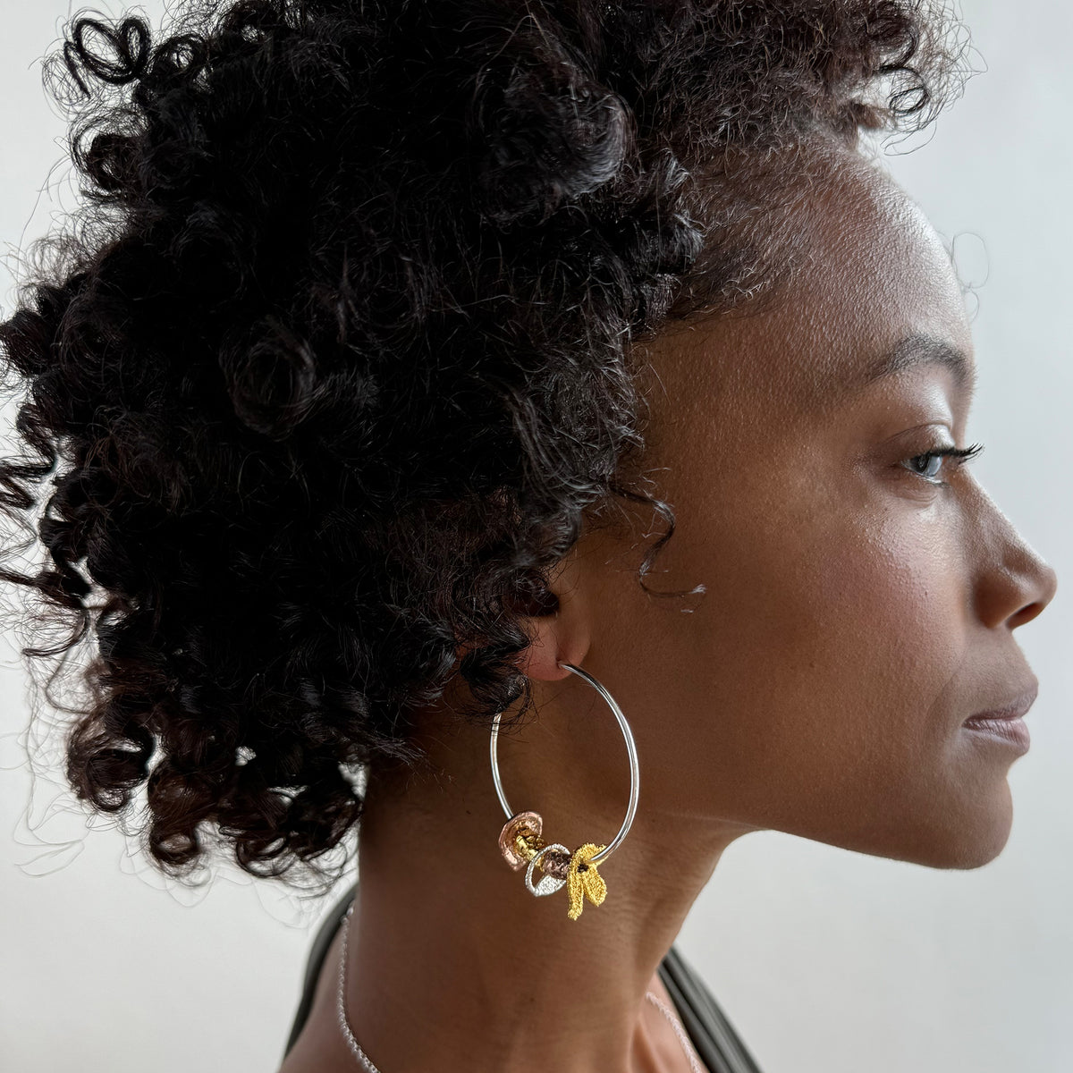 A model wearing a pair of silver hoop earrings with lace charms dipped in 24k gold, rose gold and sterling silver.