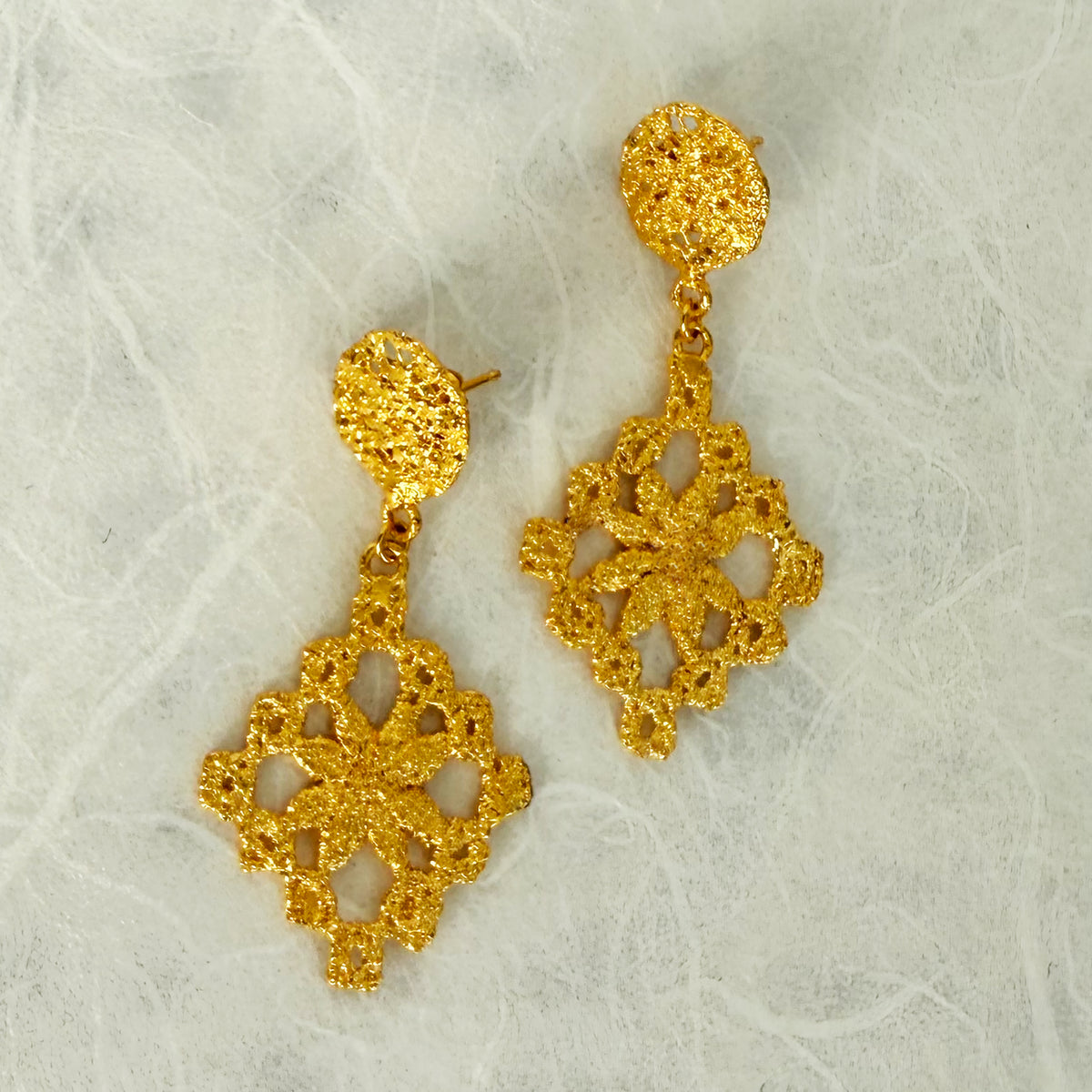 Chandelier lace earrings in 24k gold on white texturred background.