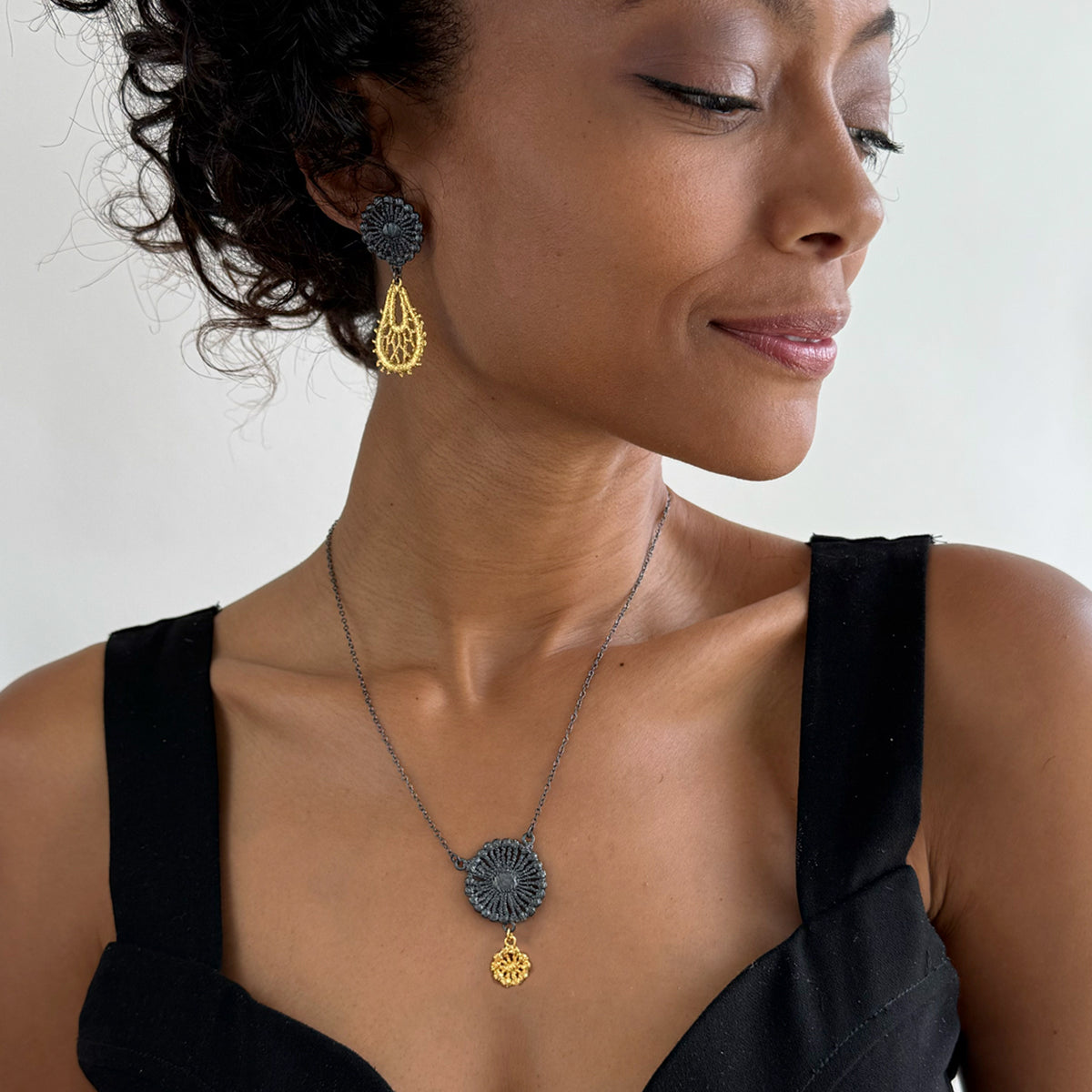 A model wearing a necklace and earrings  in 24k gold and oxidized black sterling silver.