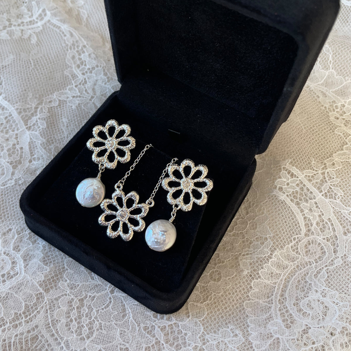 Pair of silver floral lace earrings with baroque coin pearls and floral necklace in a black suede jewelry box.