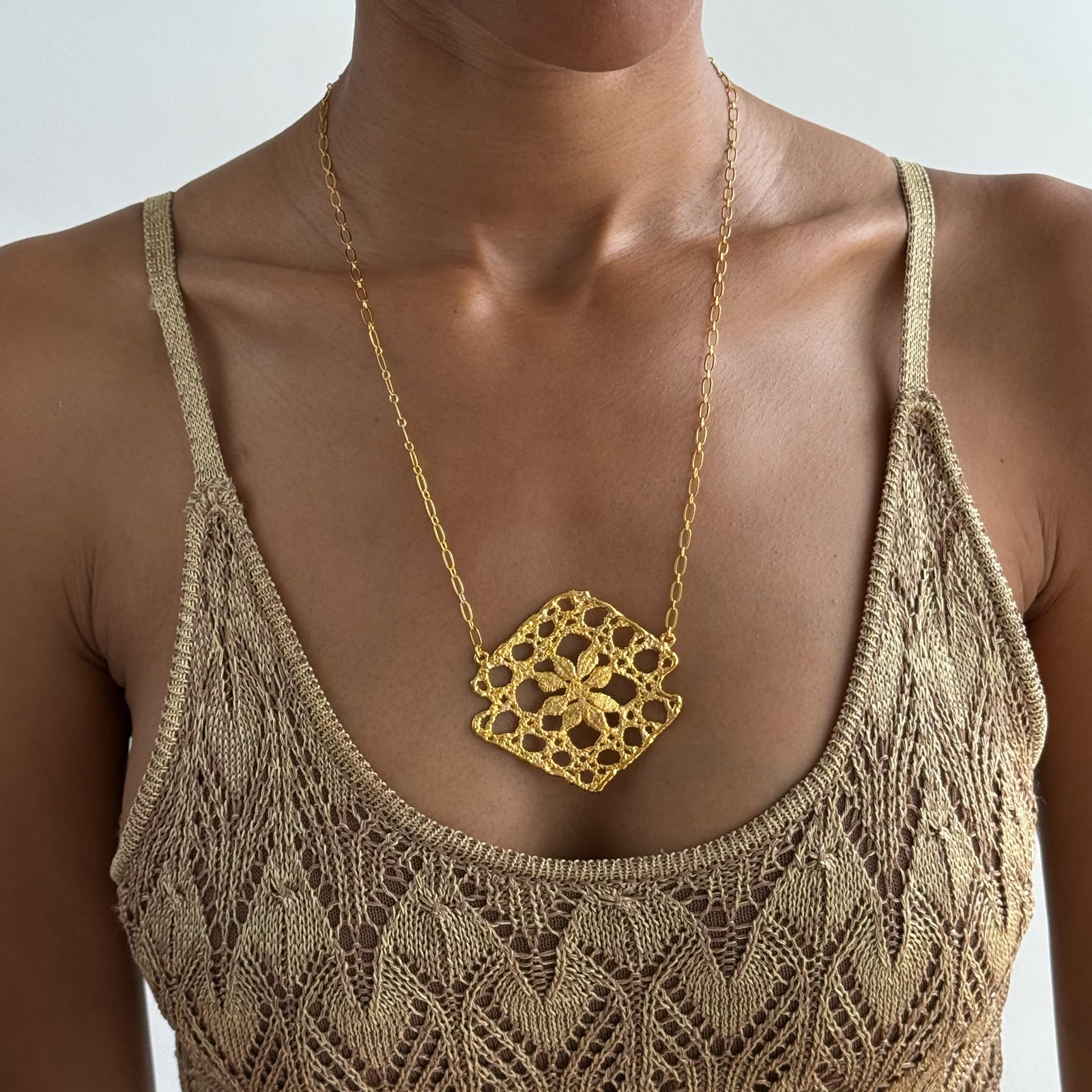 Lace pendant necklace in 24k gold on white background.