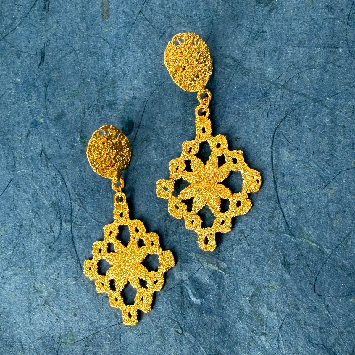 Chandelier lace earrings in 24k gold on blue background.