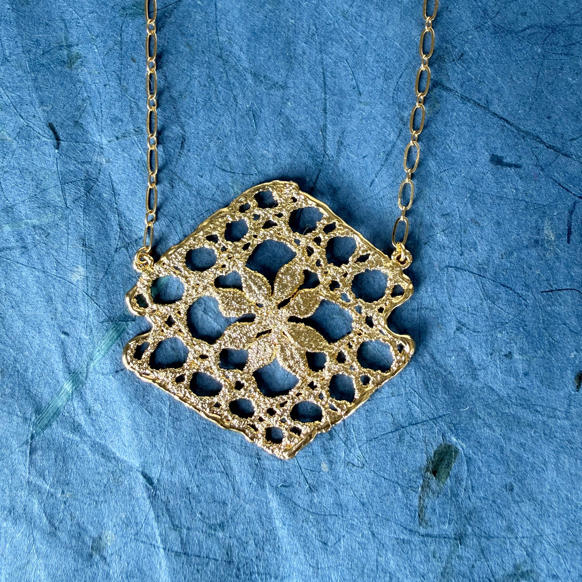 Lace pendant in 24k gold on blue background.