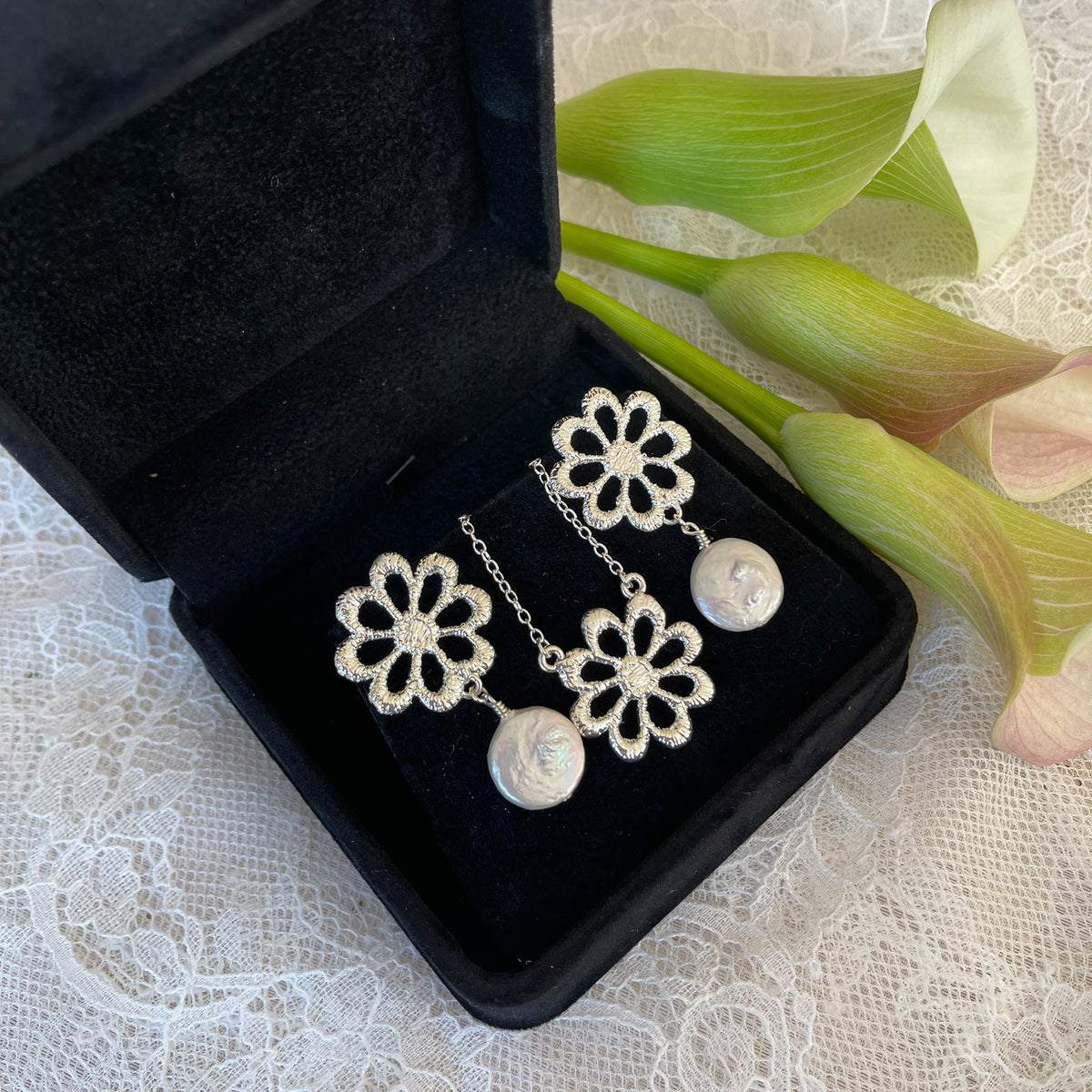 Pair of silver floral lace earrings with baroque coin pearls and floral necklace in a black suede jewelry box.