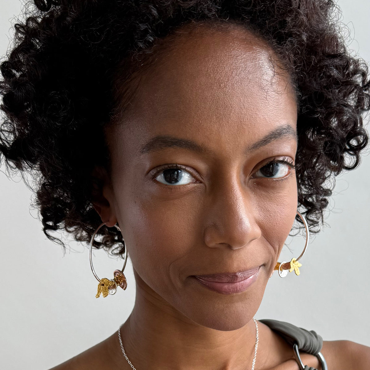 A model wearing a pair of silver hoop earrings with lace charms dipped in 24k gold, rose gold and sterling silver.