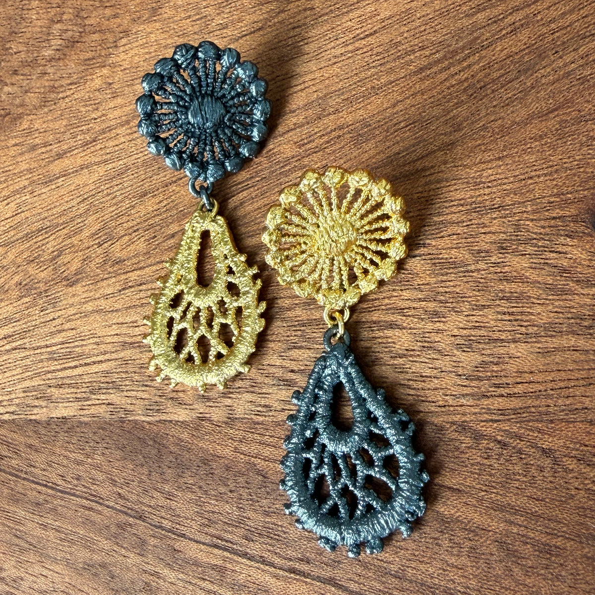 The Flora lace earrings in 24k gold and oxidized black sterling silver on a wooden surface.