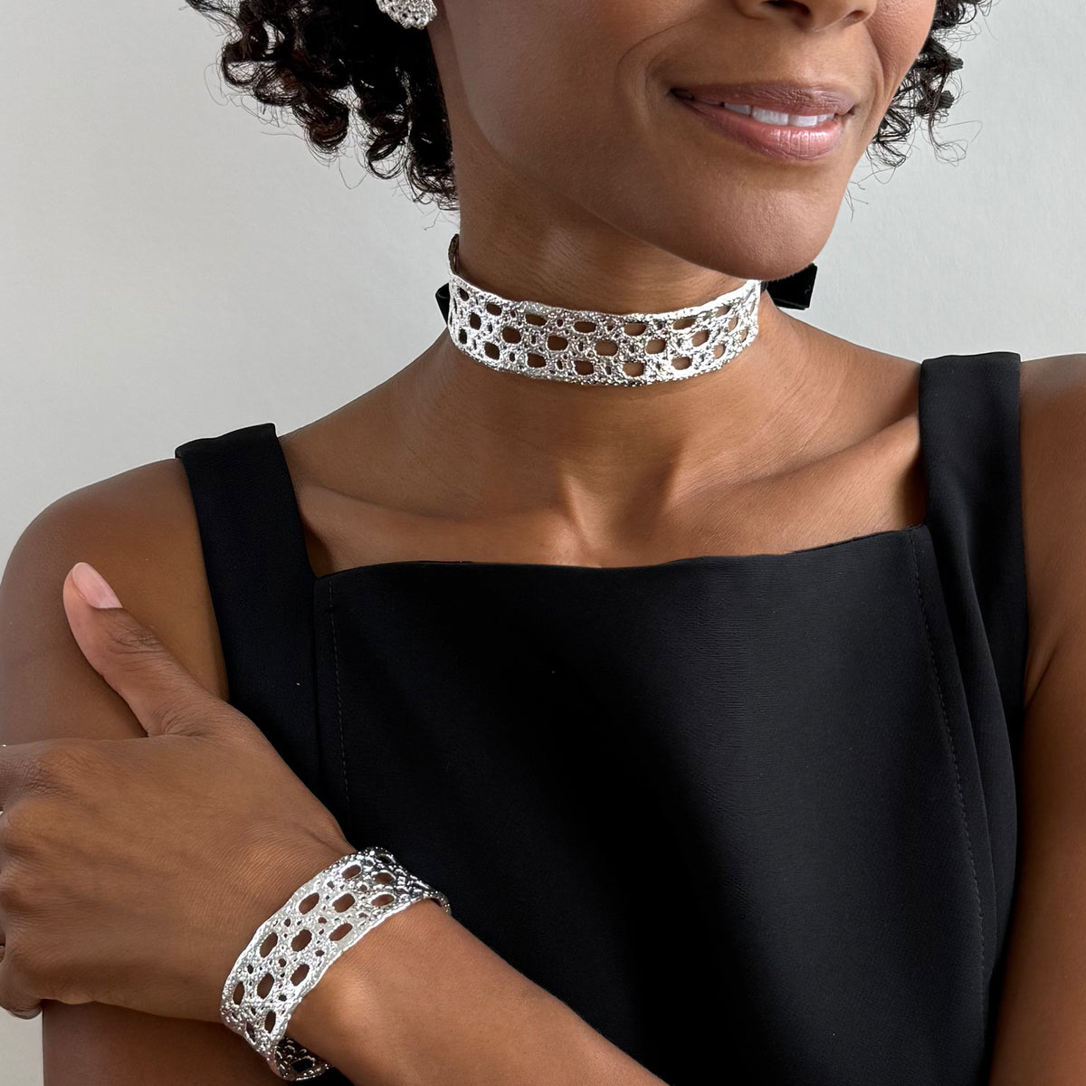 A model wearing a French lace choker in sterling silver with velvet ribbons and a matching lace sterling silver cuff bracelet.