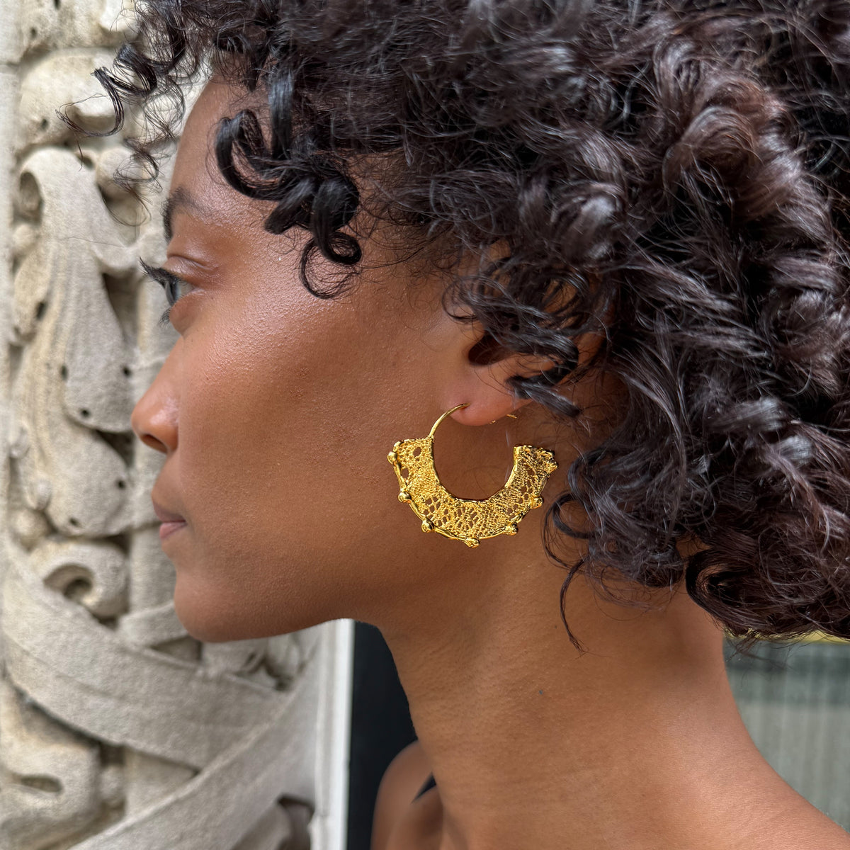 Model wearing Violette 24k gold hoop earrings with intricate designs.