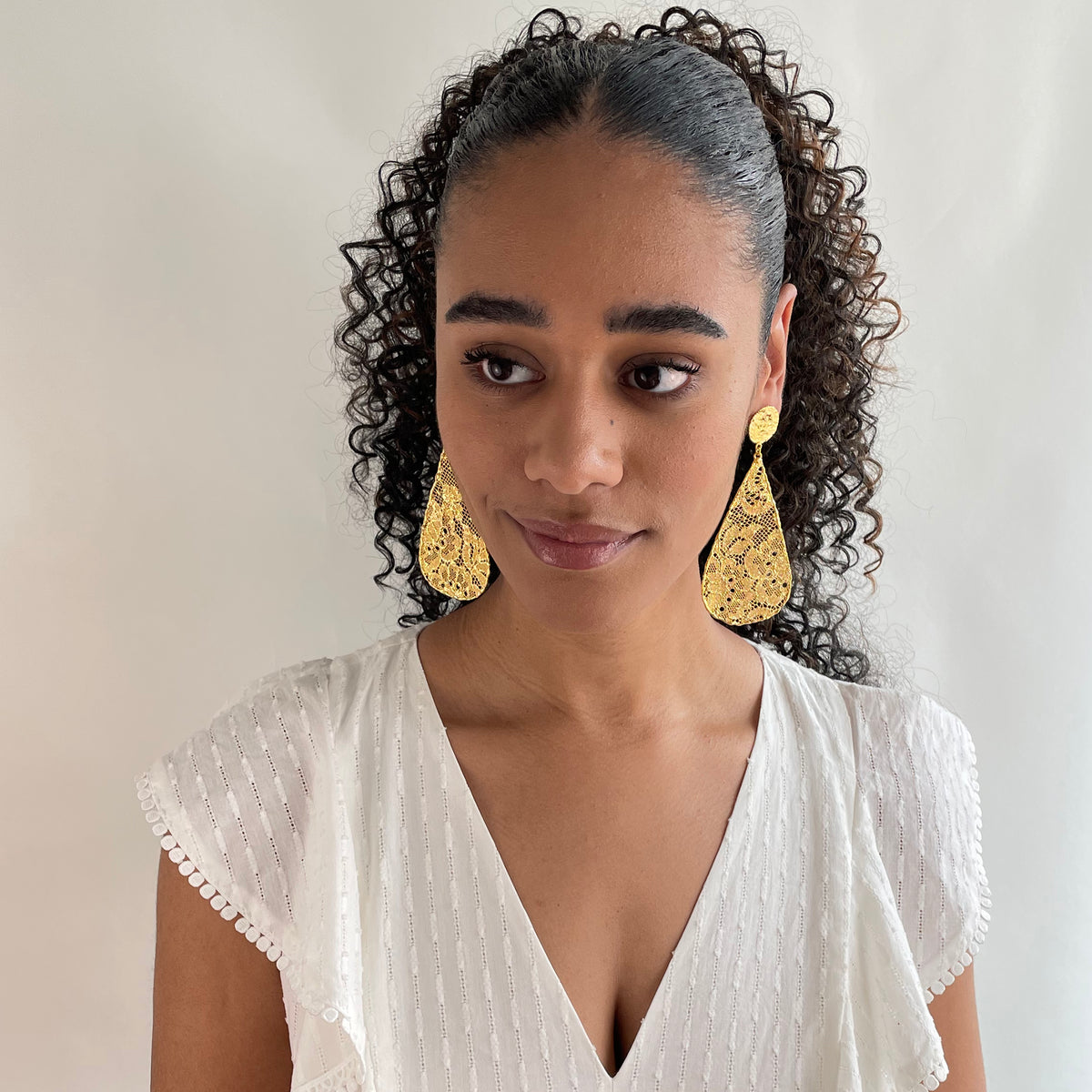 Large lace teardrop earrings dipped in 24k gold on a model.
