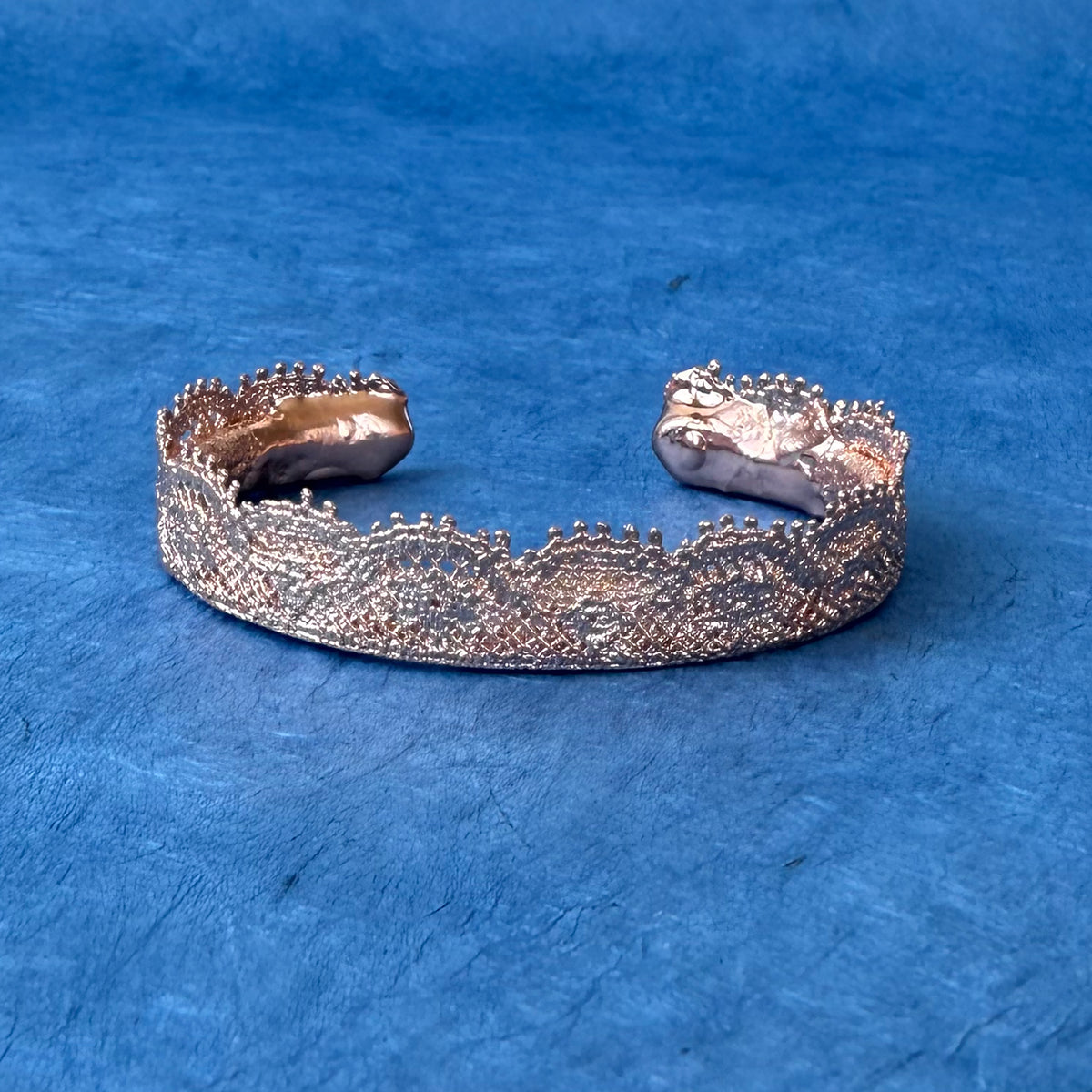 Lace bangle bracelet in dipped rose gold on blue background.