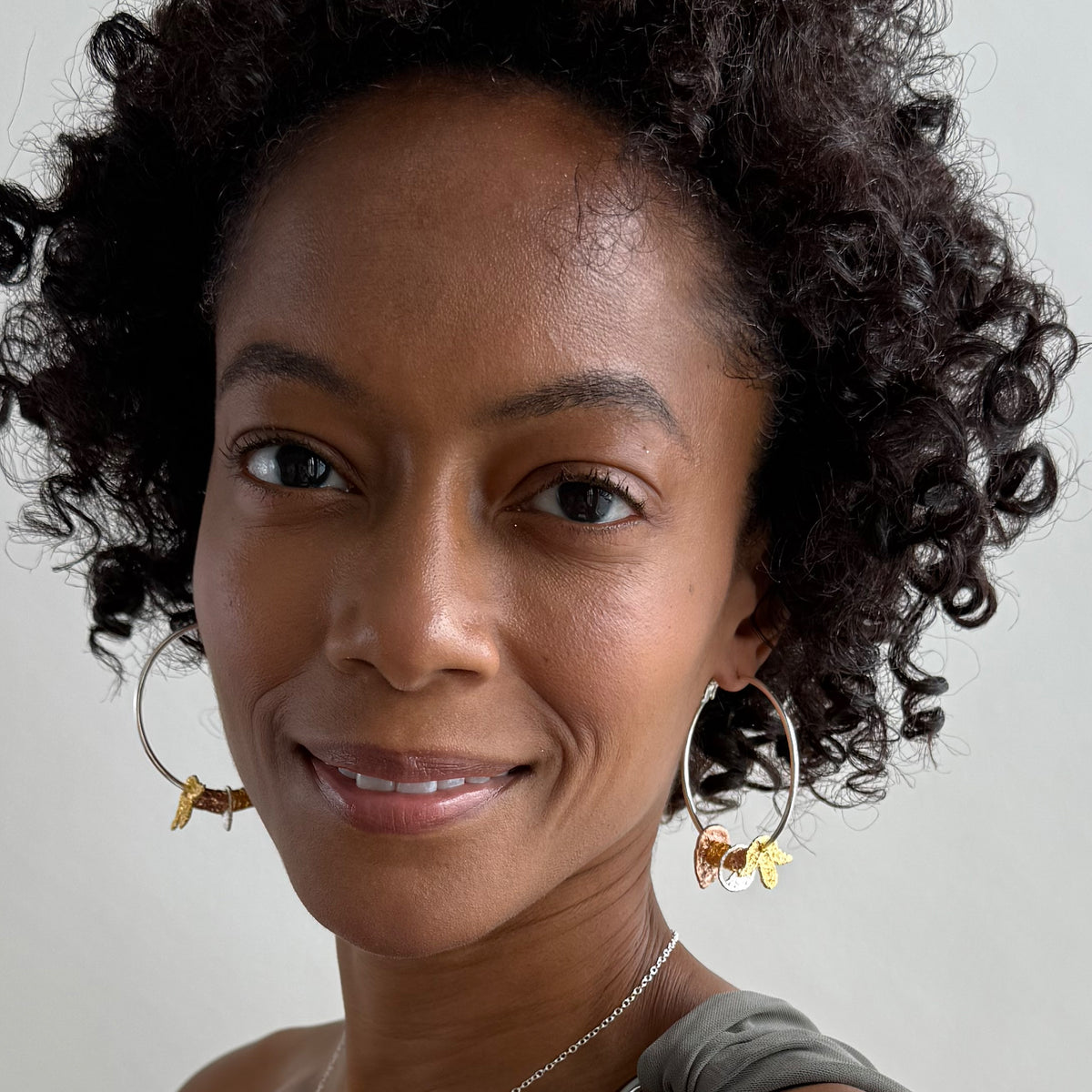 A model wearing a pair of silver hoop earrings with lace charms dipped in 24k gold, rose gold and sterling silver.