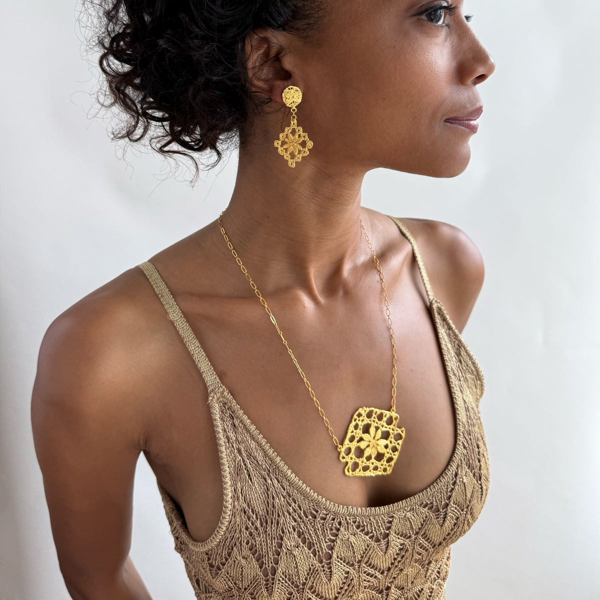 Model wearing lace pendant necklace and lace earrings, both in 24k gold.