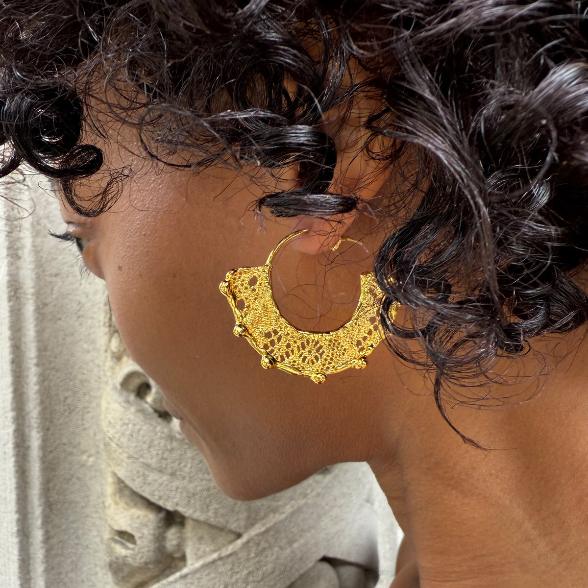 Model wearing Violette 24k gold hoop earrings with intricate designs.