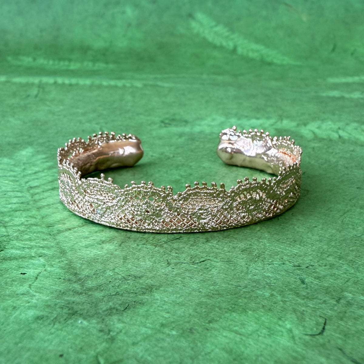 Lace bangle bracelet in dipped rose gold on bright green background. 