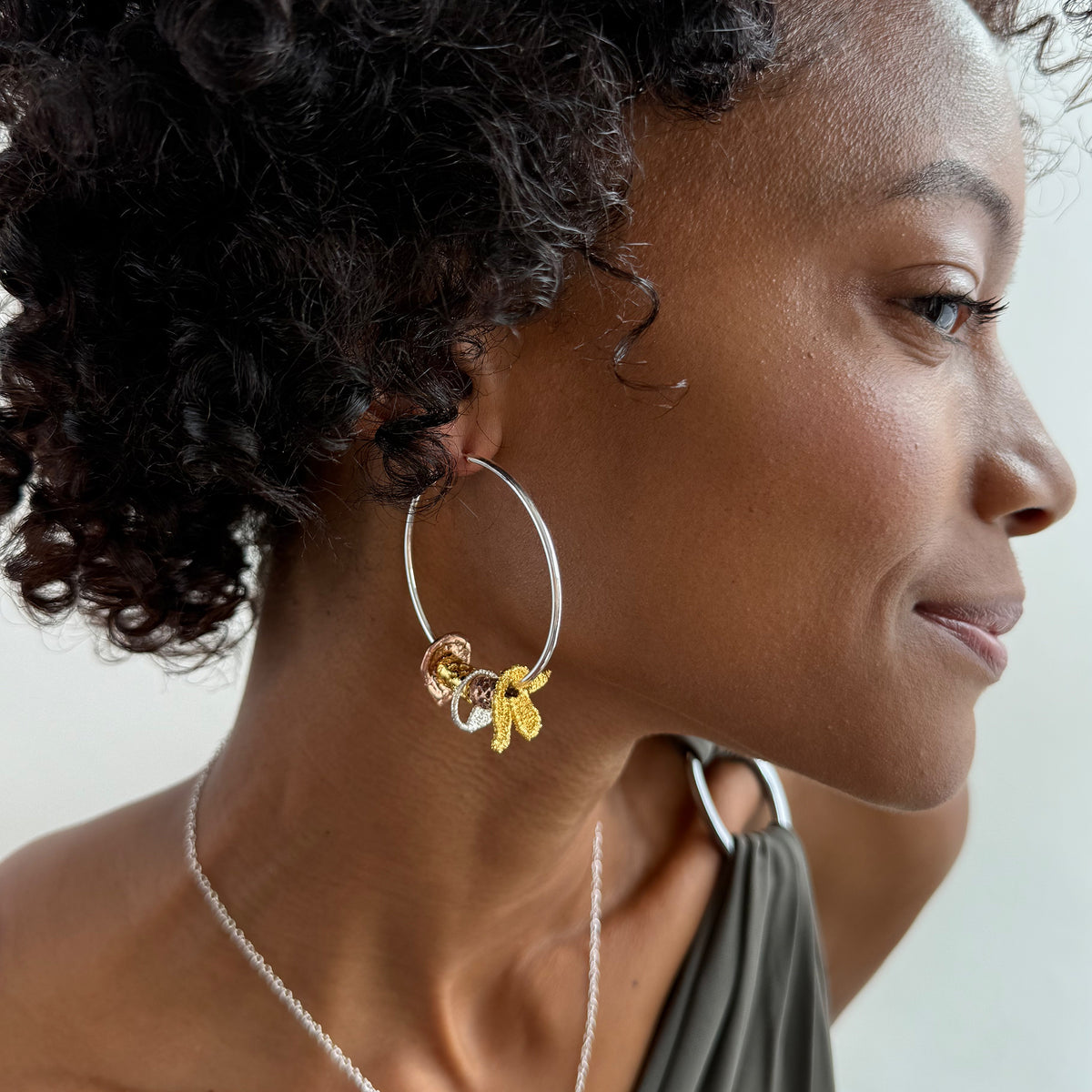 A model wearing a pair of silver hoop earrings with lace charms dipped in 24k gold, rose gold and sterling silver.