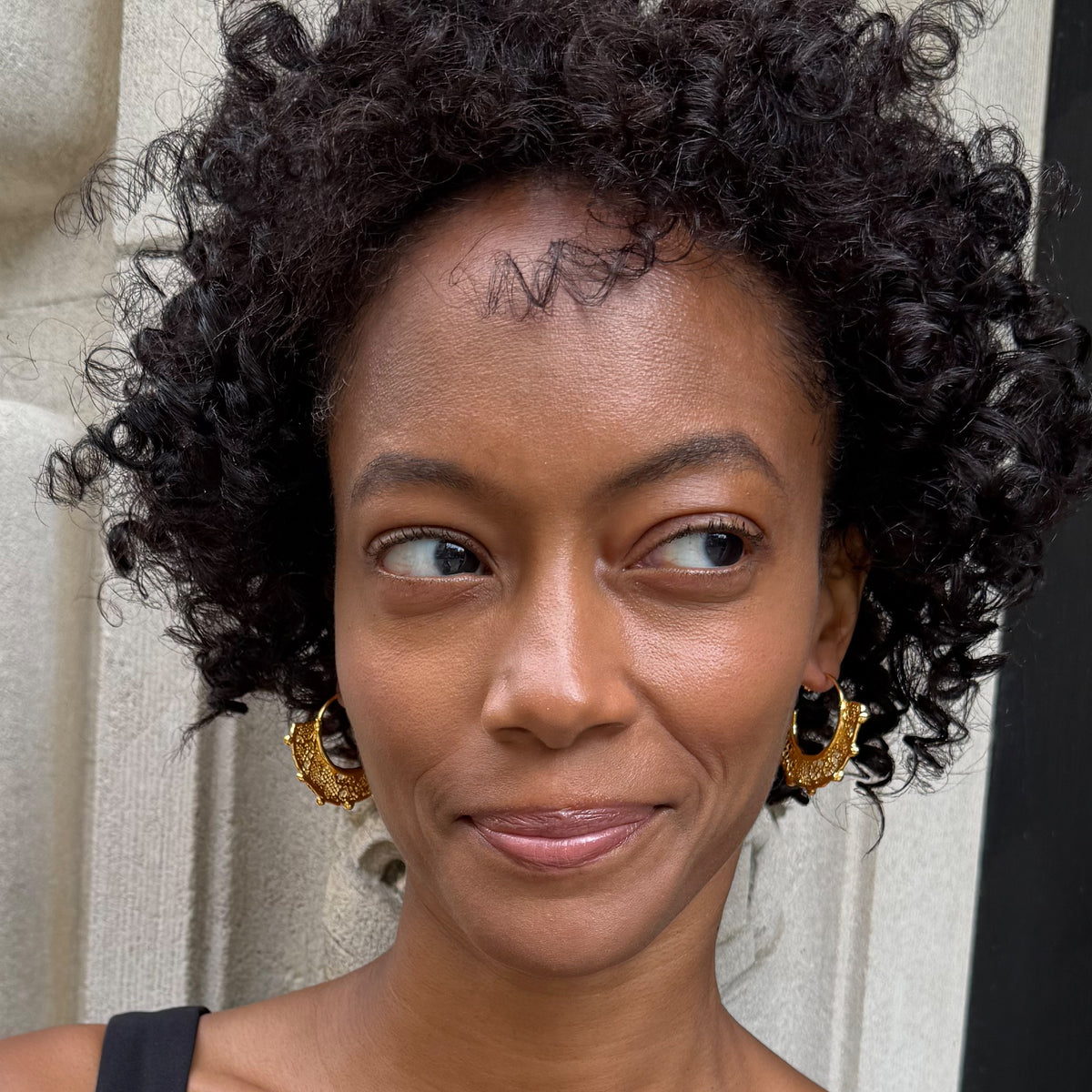 Model wearing Violette 24k gold hoop earrings with intricate designs.