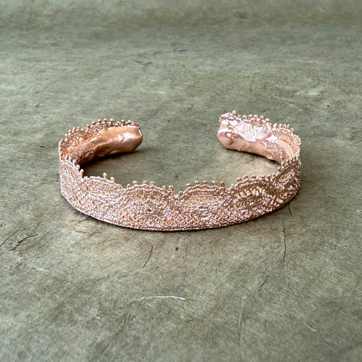 Lace bangle bracelet in dipped rose gold on grey green background.