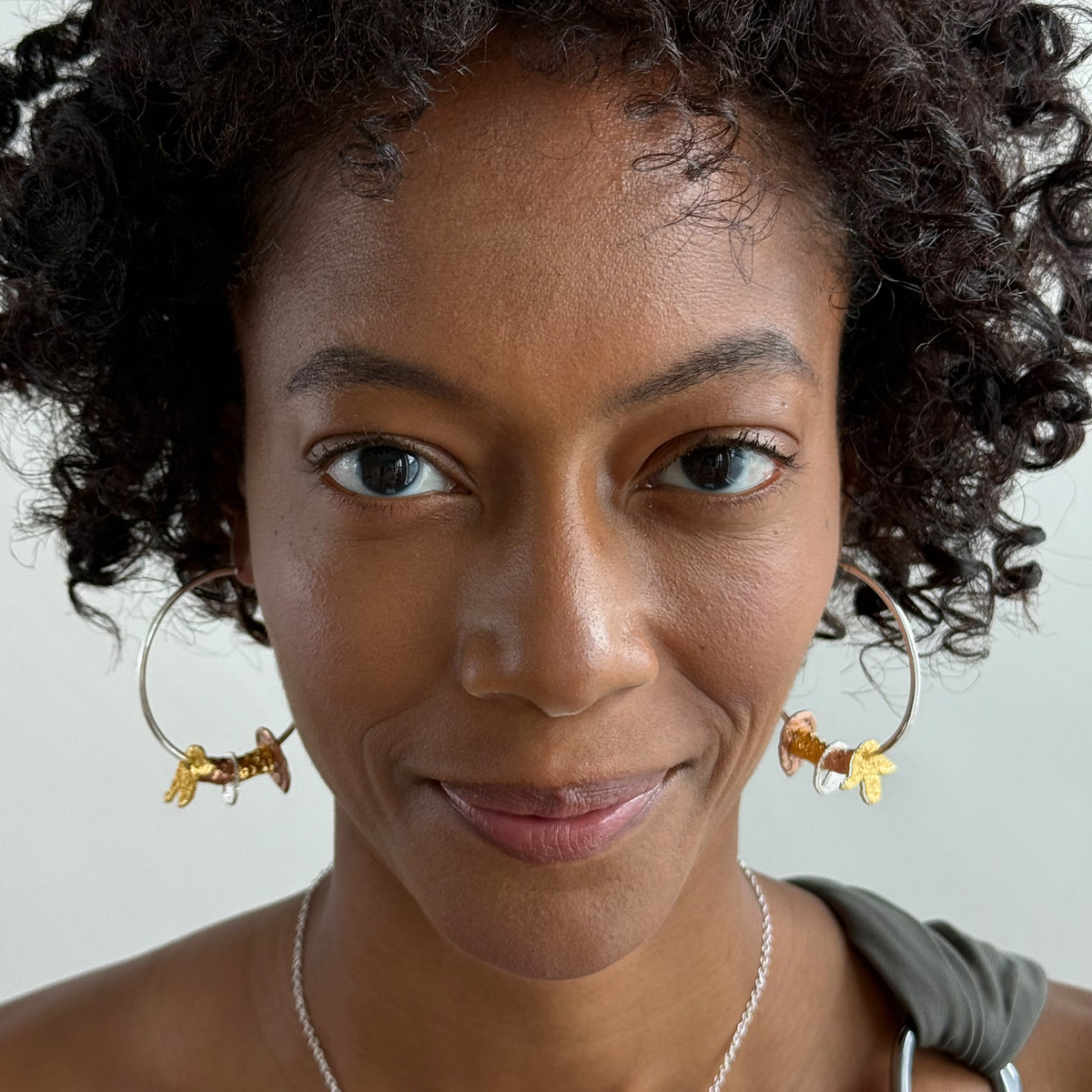 A model wearing a pair of silver hoop earrings with lace charms dipped in 24k gold, rose gold and sterling silver.