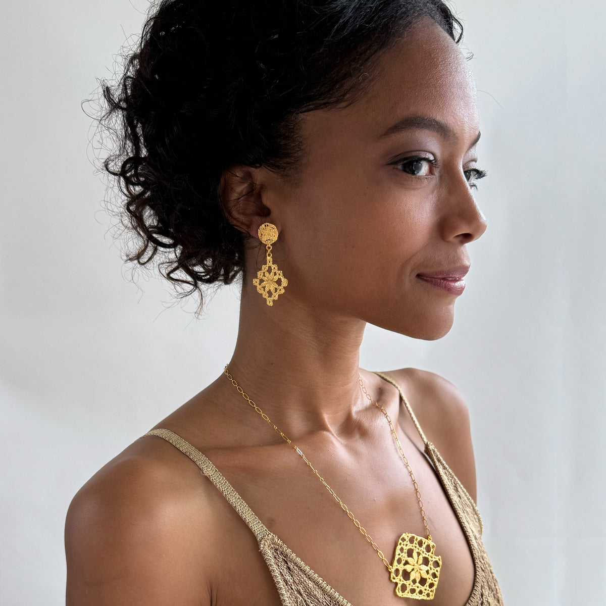 Model wearing chandelier lace earrings and lace pendant necklace, both in 24k gold.