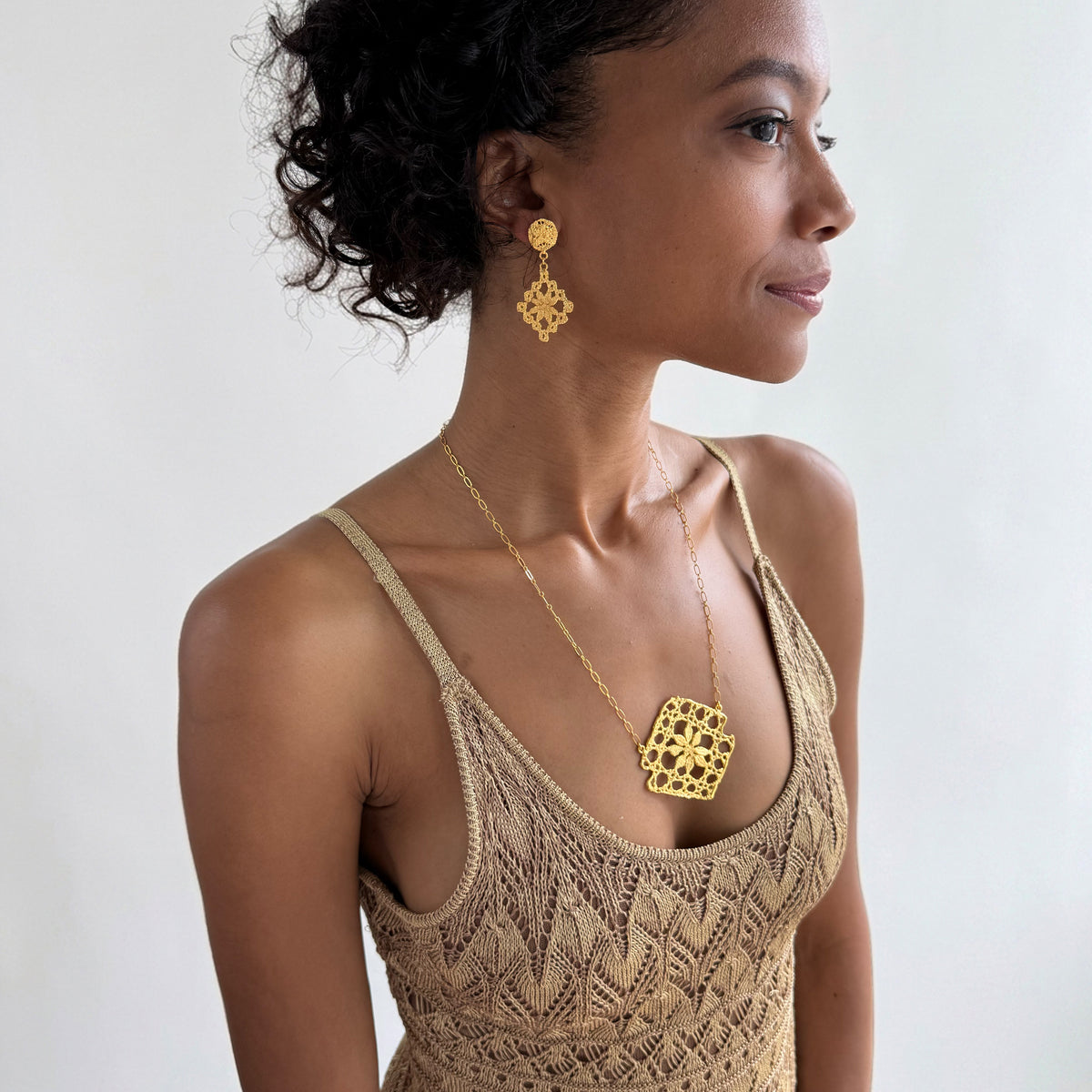 Model wearing lace pendant necklace and lace earrings, both in 24k gold.