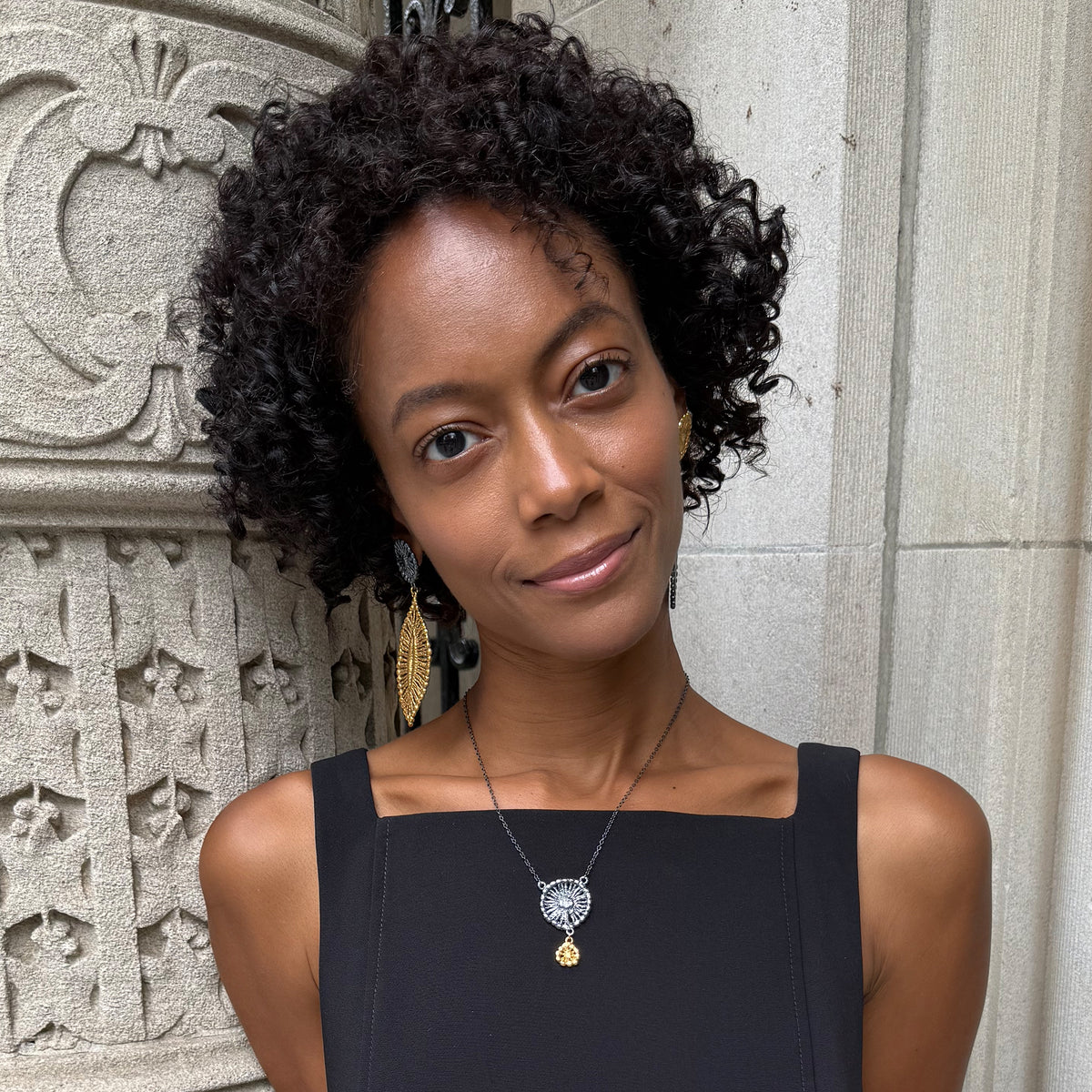 A model wearing necklace with black oxidized flower silver pendant and 24k gold charm.