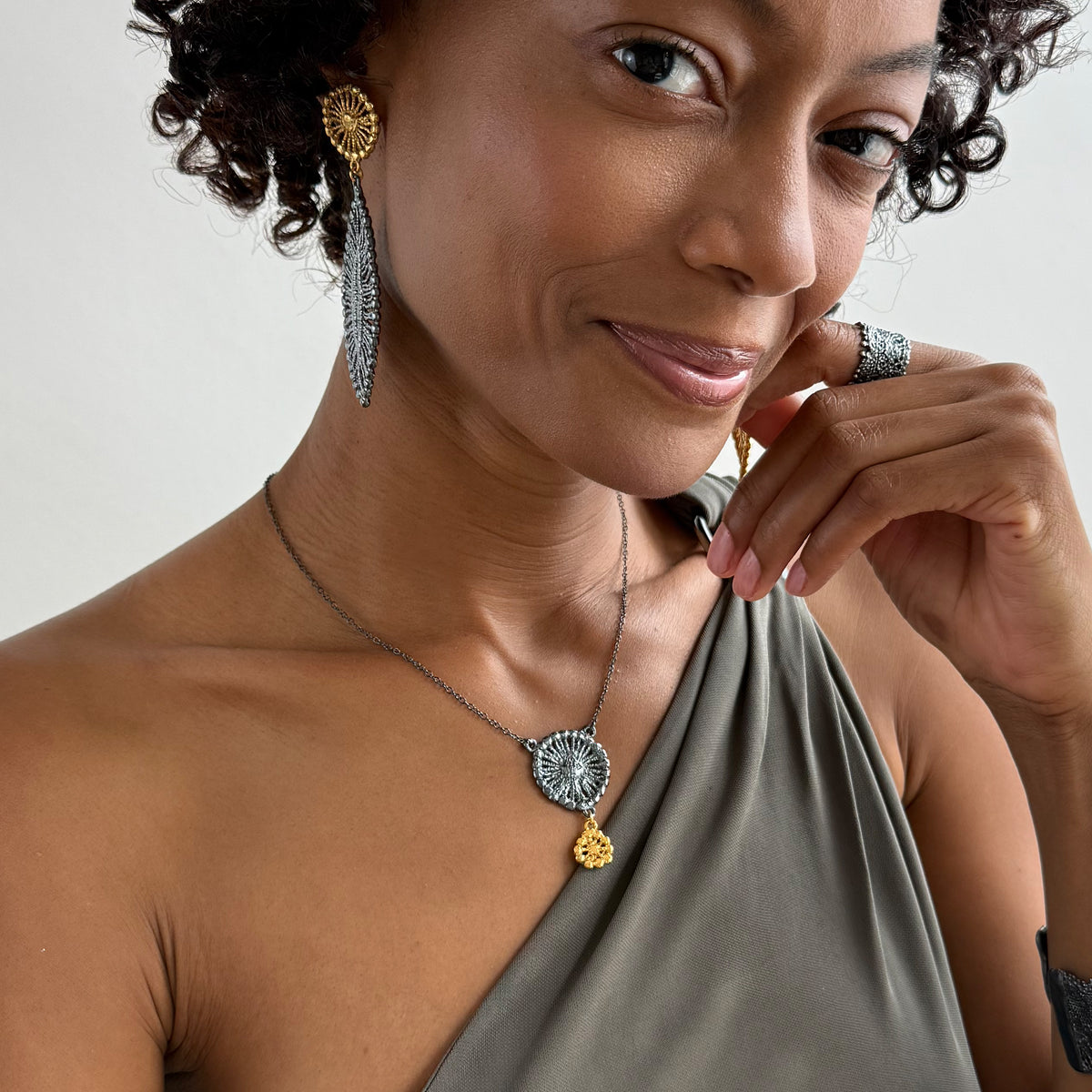 A model wearing necklace with black oxidized flower silver pendant and 24k gold charm.