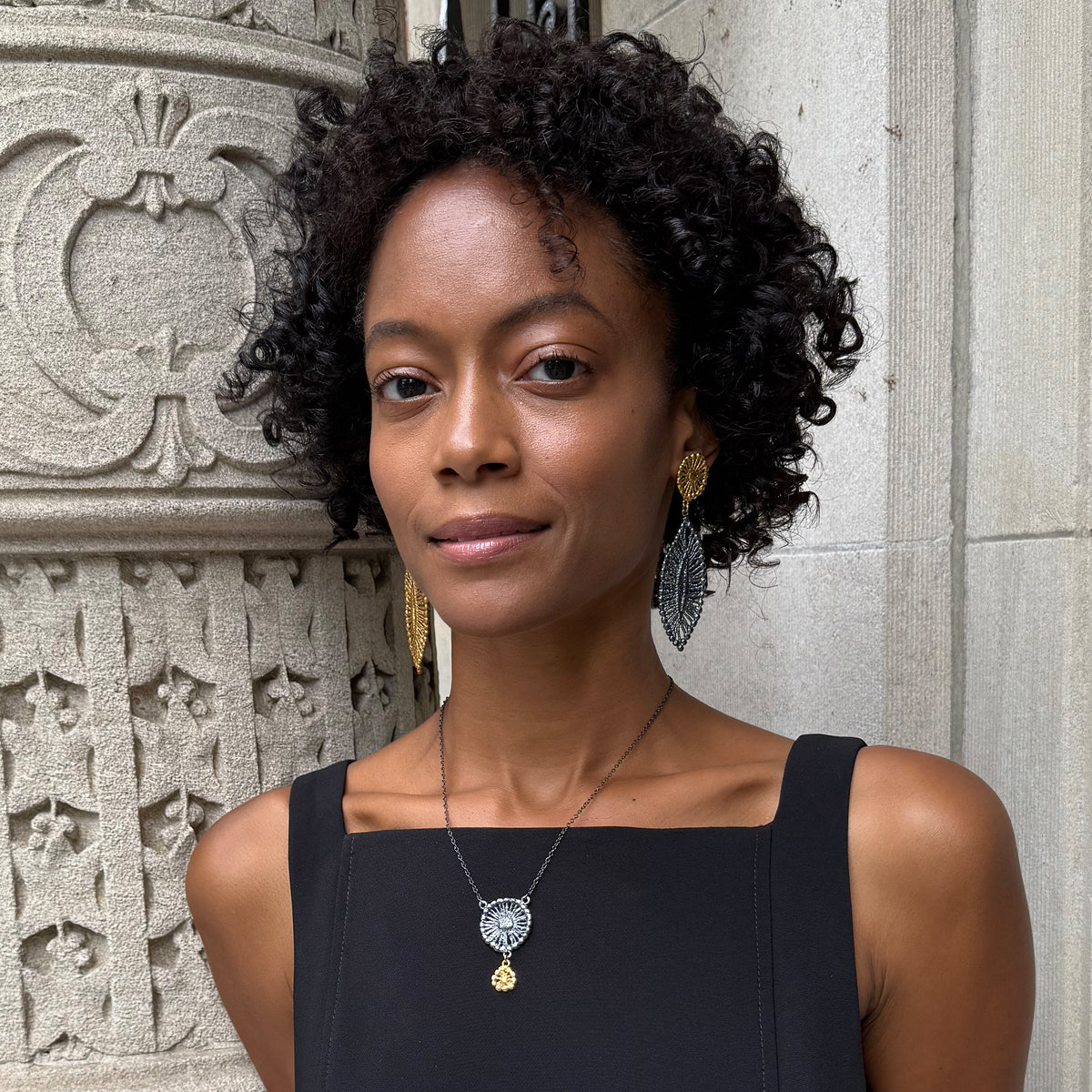 A model wearing necklace with black oxidized flower silver pendant and 24k gold charm.
