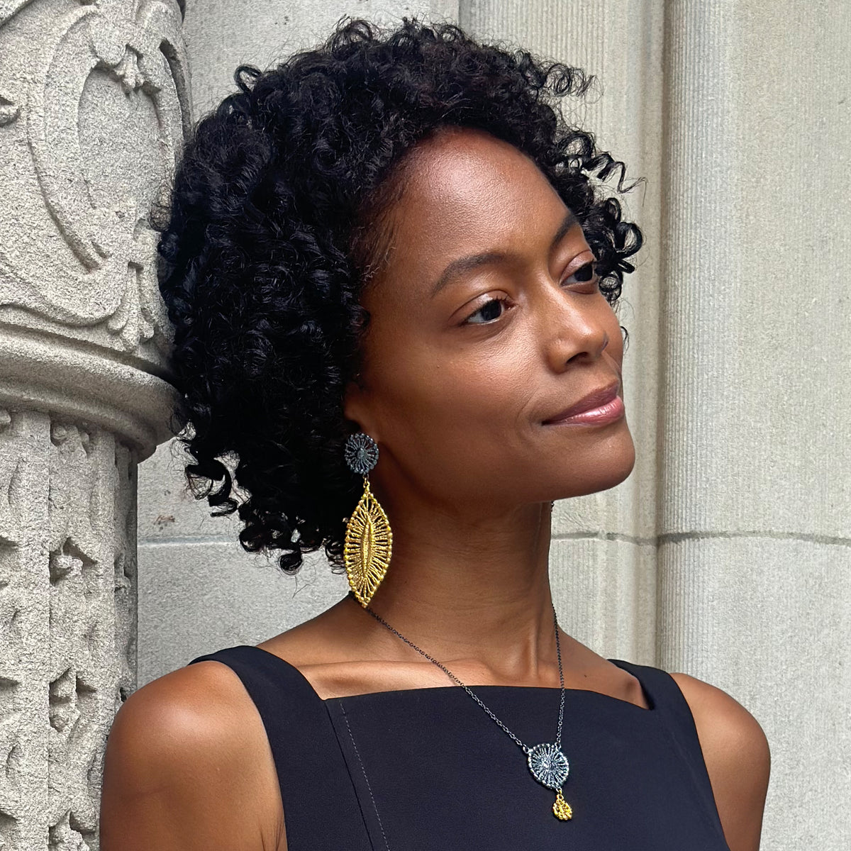 A model wearing a pair of leaf shaped 24k gold and black oxidized sterling silver earrings.