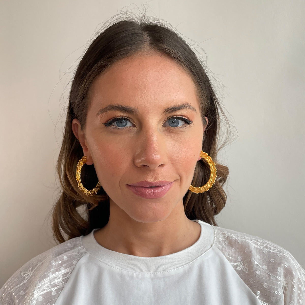 Jacqueline large lace hoop earrings in 24k gold on a model.