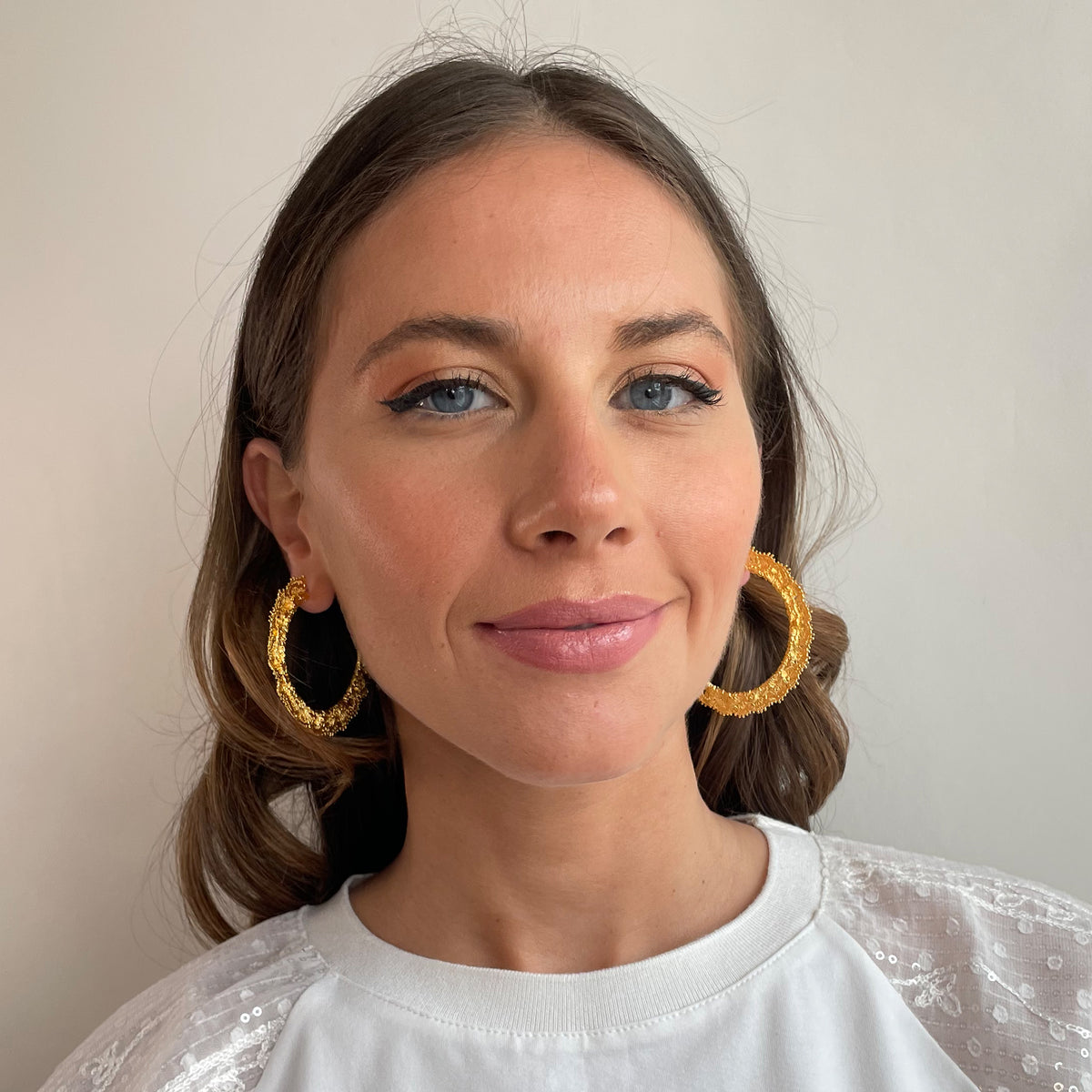 Jacqueline large lace hoop earrings in 24k gold on a model.