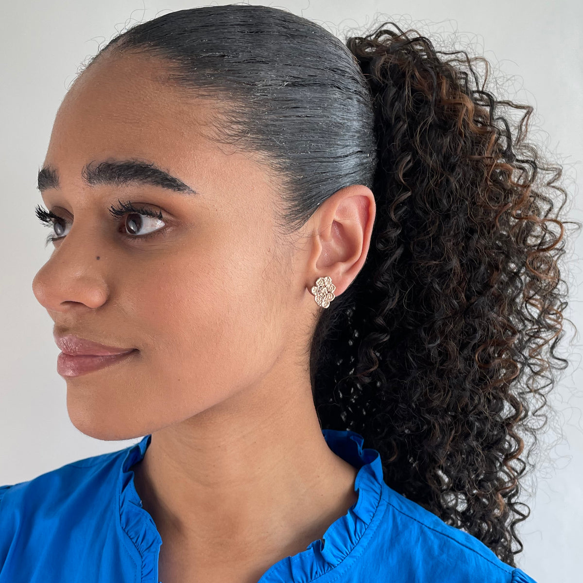 Small, exquisite stud earring in the shape of a lace flower dipped in rose gold on a model.