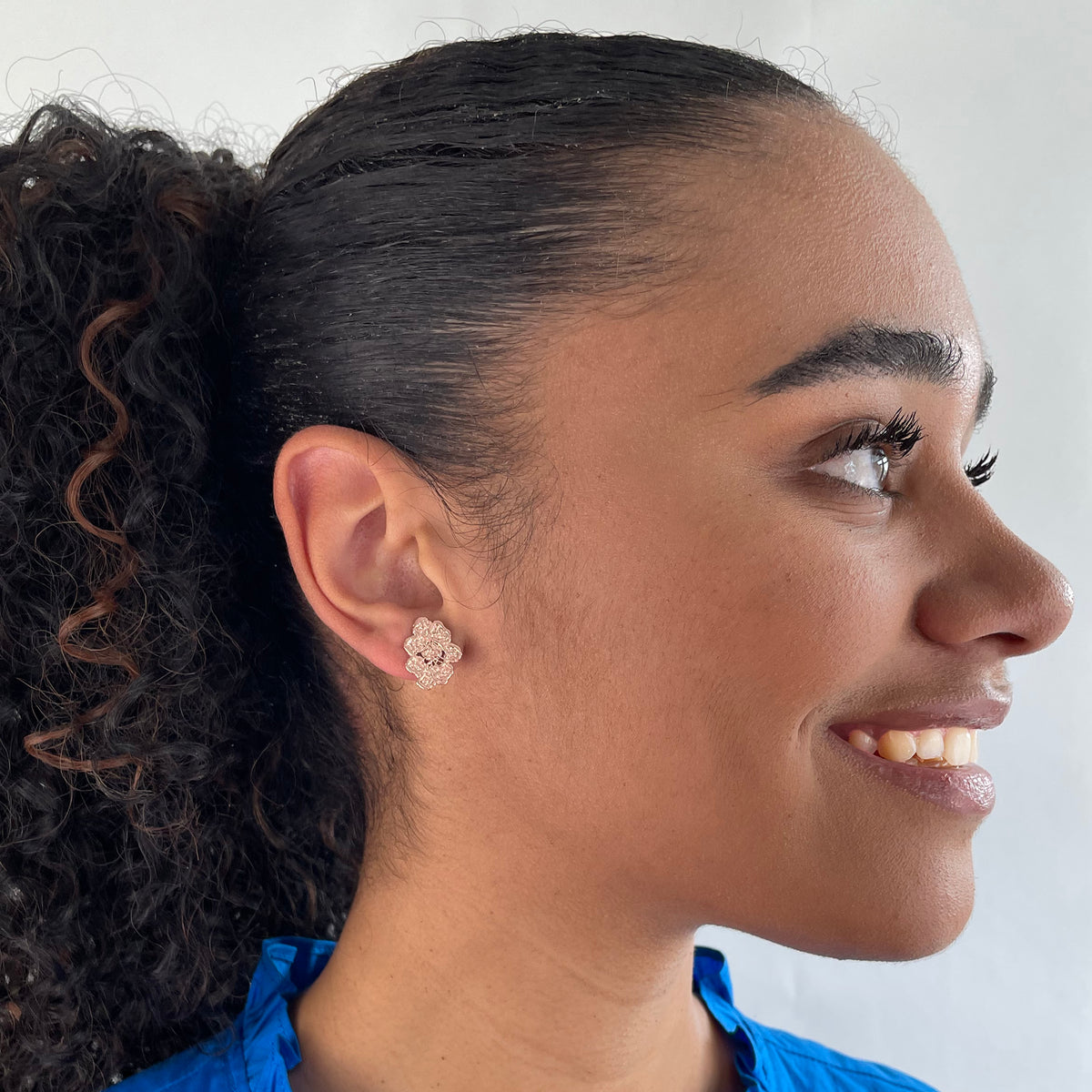 Small, exquisite stud earring in the shape of a lace flower dipped in rose gold on a model.