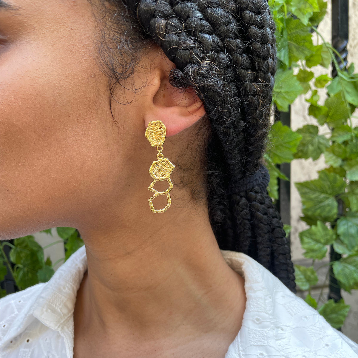 Honeycomb lace drop earrings in 24k gold on a model.