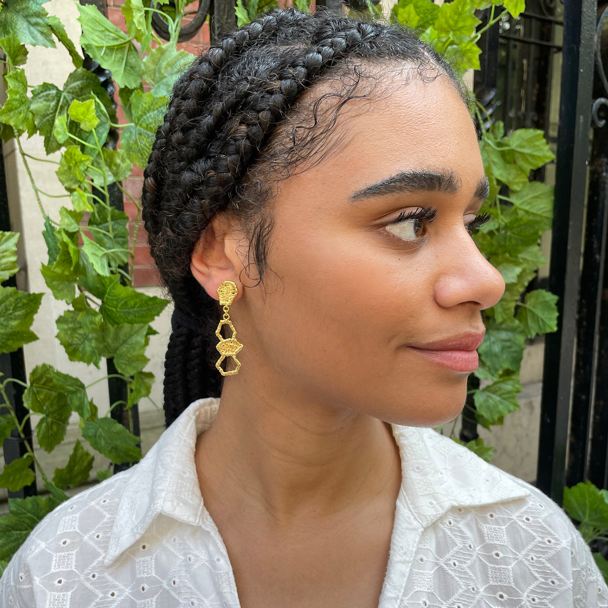 Honeycomb lace drop earrings in 24k gold on a model.