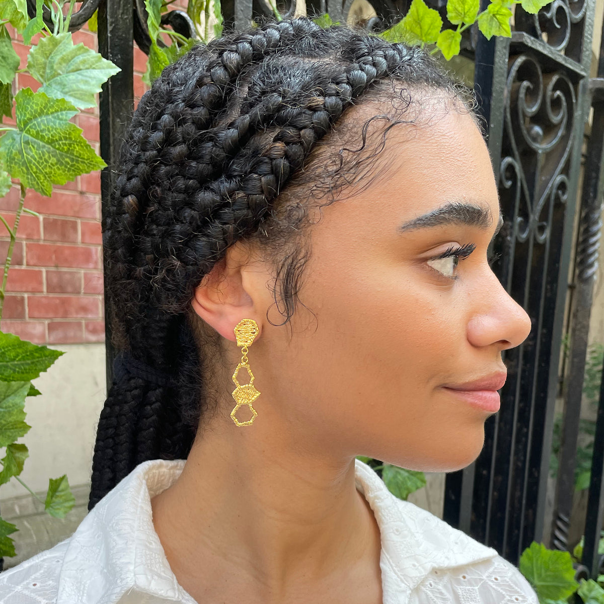 Honeycomb lace drop earrings in 24k gold on a model.
