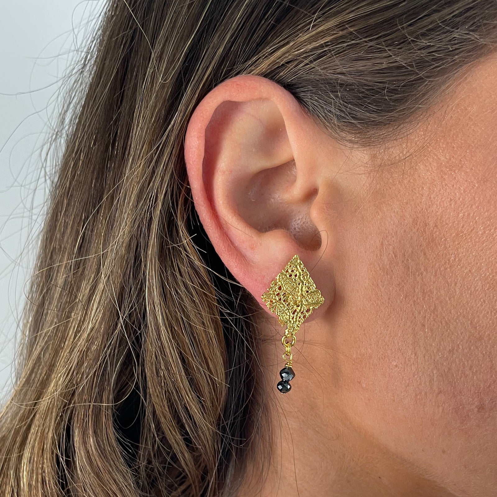 Diamond shaped lace earrings in 24k gold with two faceted black diamonds.
