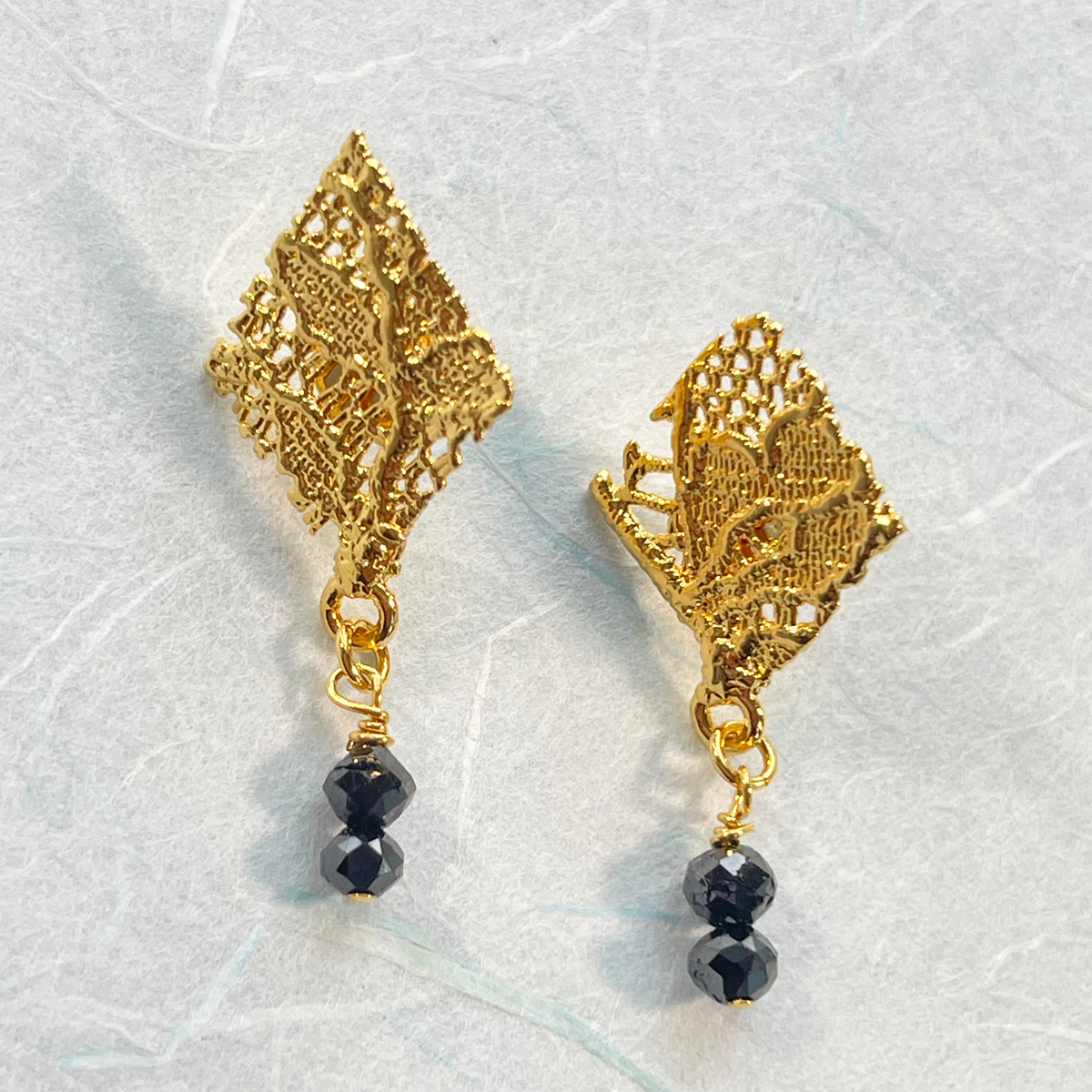 Diamond shaped lace earrings in 24k gold with two faceted black diamonds.