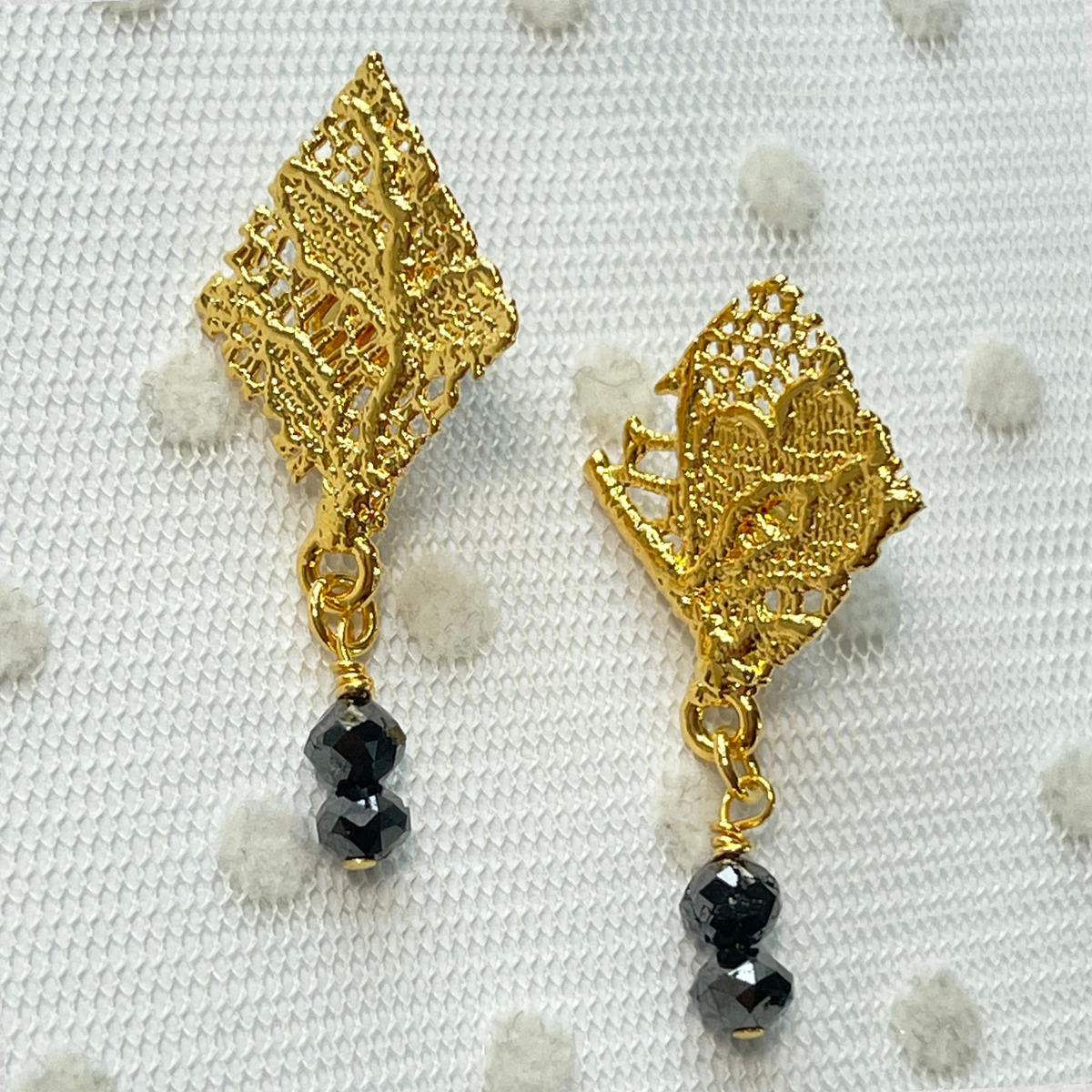 Diamond shaped lace earrings in 24k gold with two faceted black diamonds.