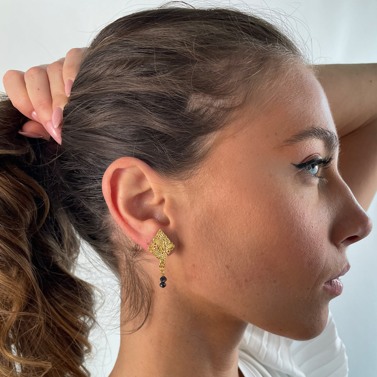 Diamond shaped lace earrings in 24k gold with two faceted black diamonds on a model.