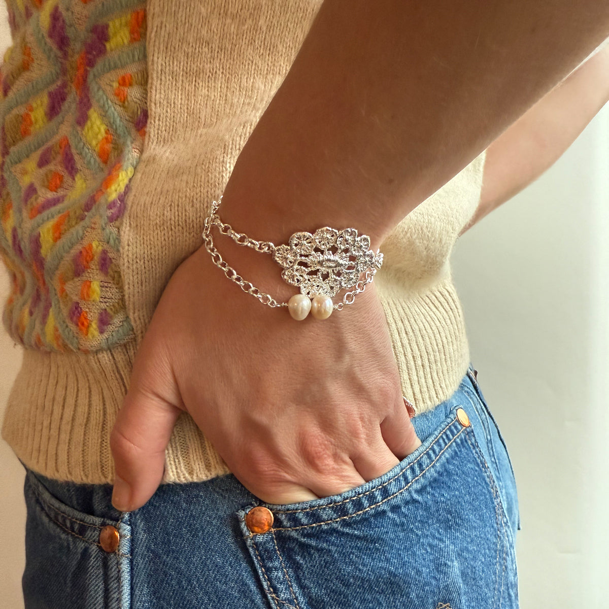 Model wearing and exquisite chain bracelet with lace medaillon in sterling silver and two white pearls.