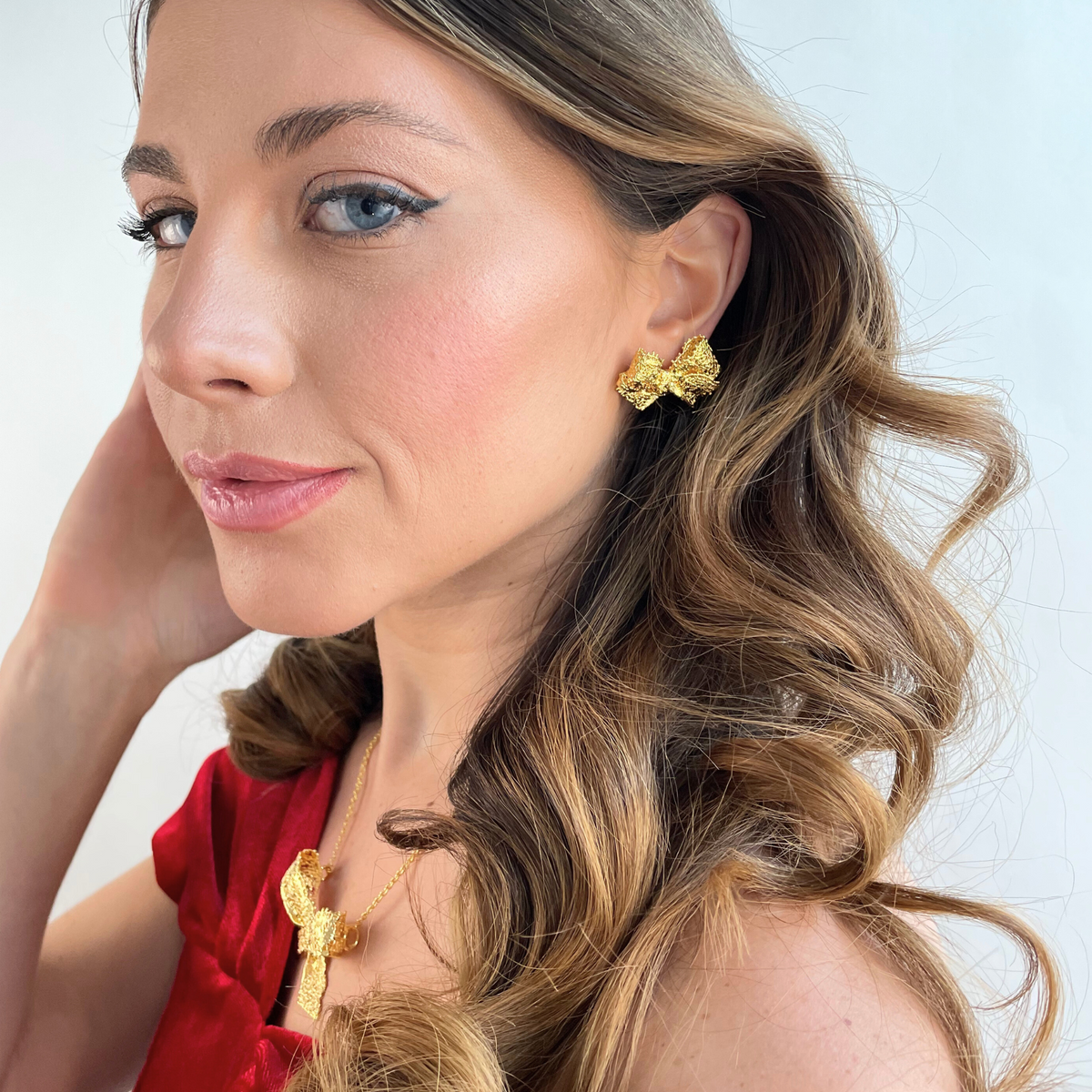 Millie lace bow earrings in 24k gold worn by a model.