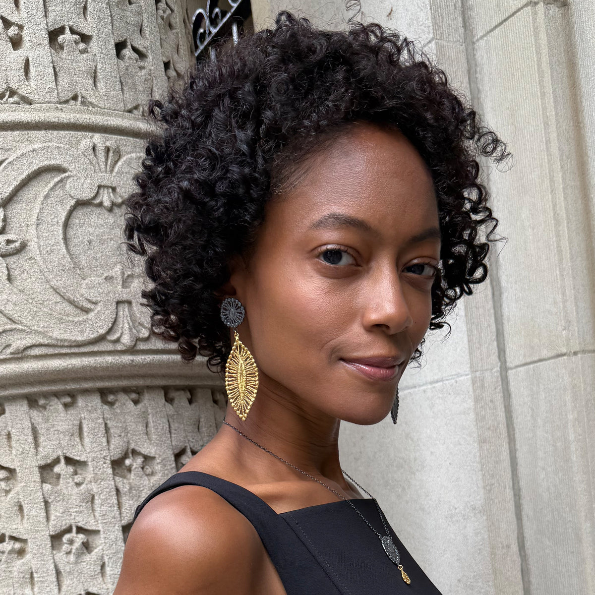 A model wearing a pair of leaf shaped 24k gold and black oxidized sterling silver earrings.