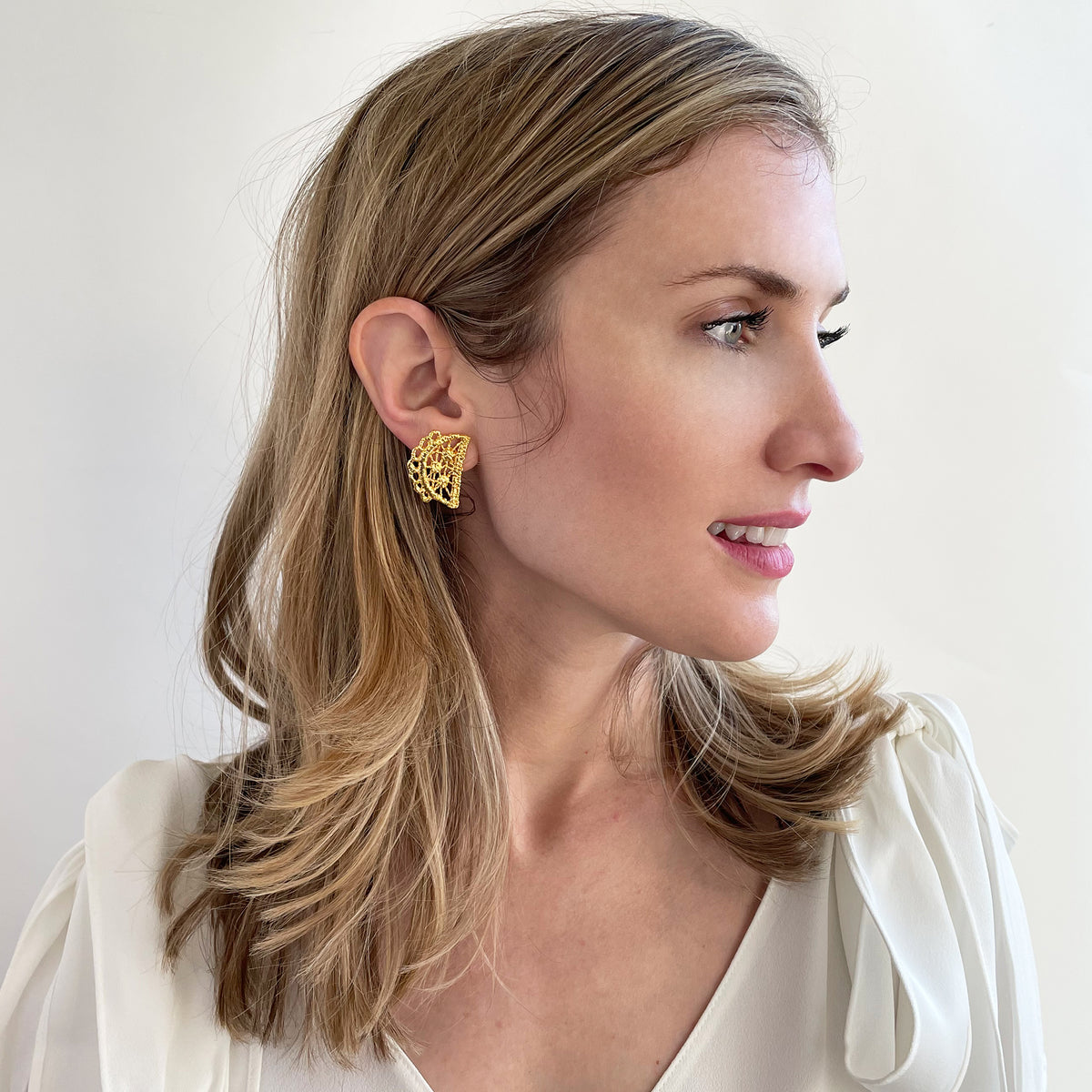 Half-moon lace stud earrings in 24k gold on a model.