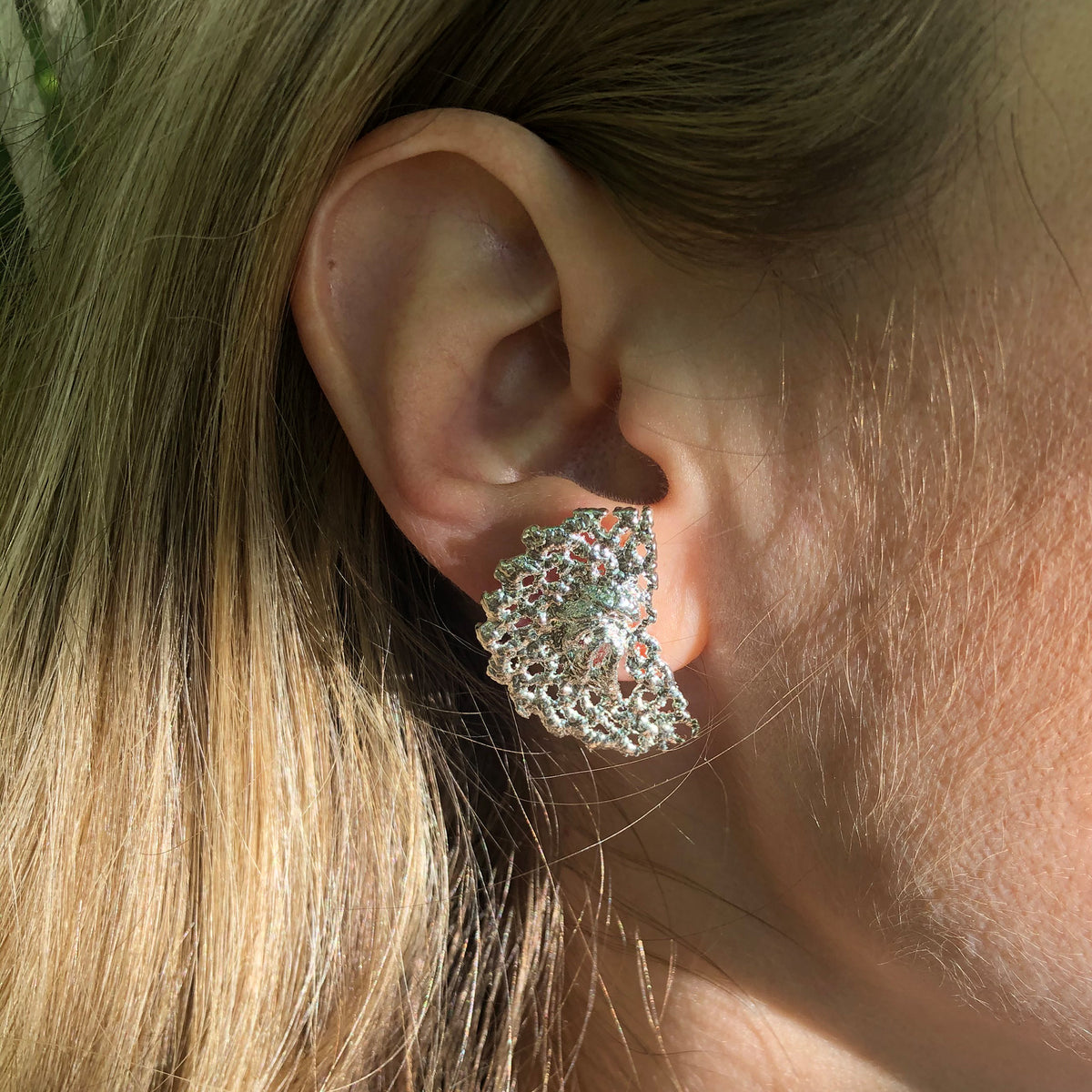 Model wearing half moon stud earrings made from Swedish lace dipped in sterling silver.