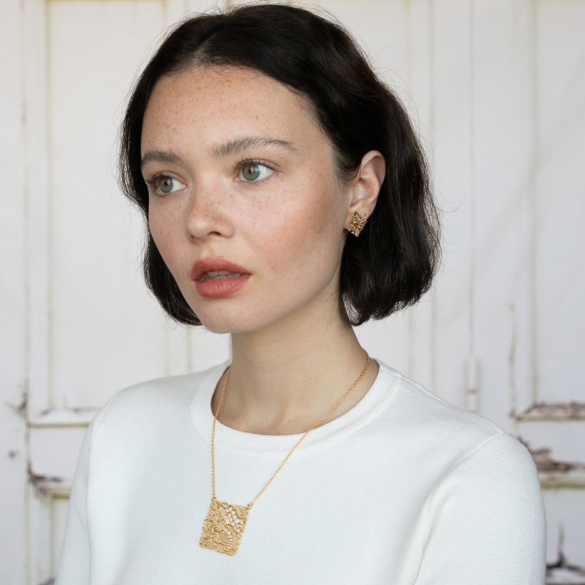 Intricate square pendant lace necklace in 24k gold worn by a model.