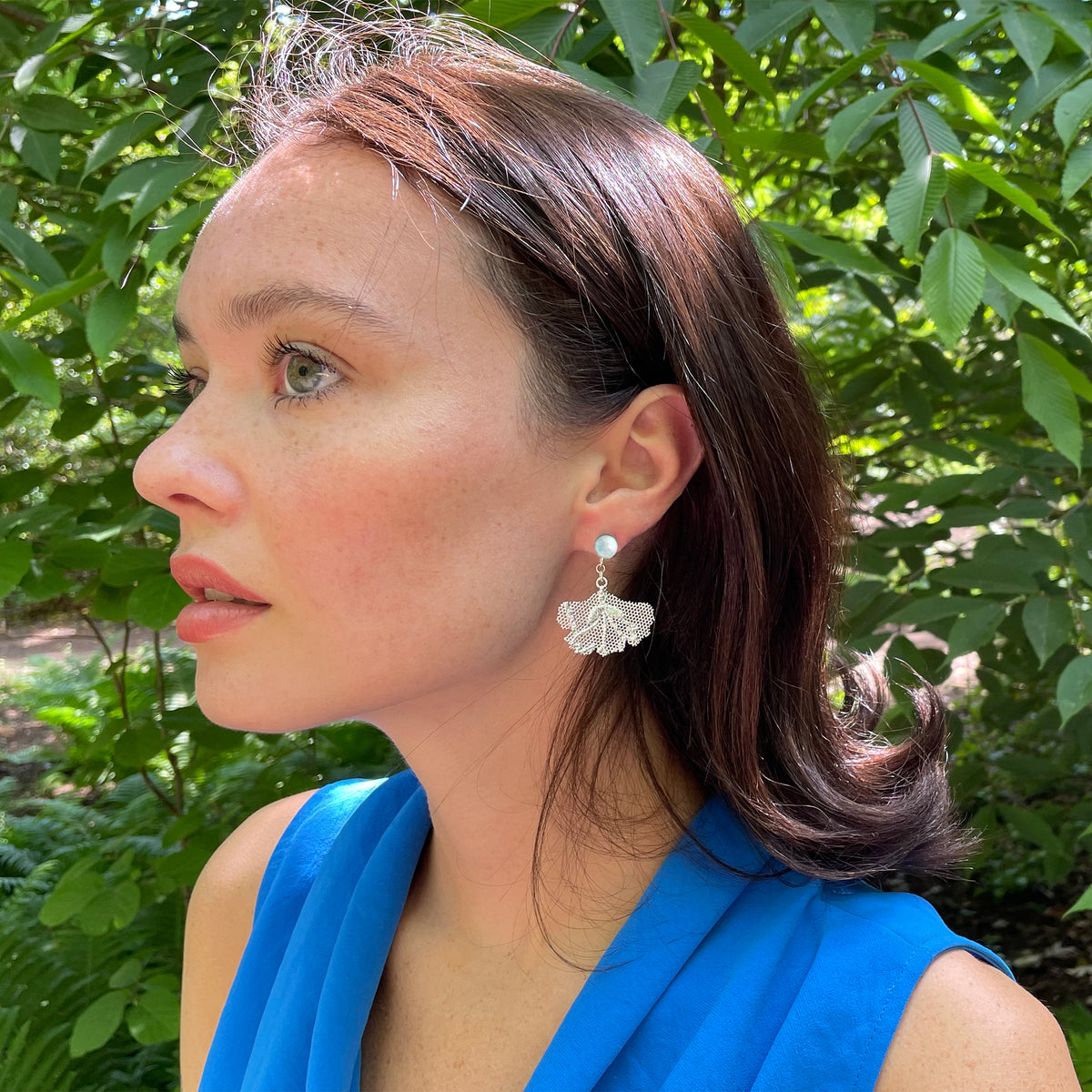 Model wearing pearl earrings with lace in the shape of a ginkgo leaf in sterling silver.