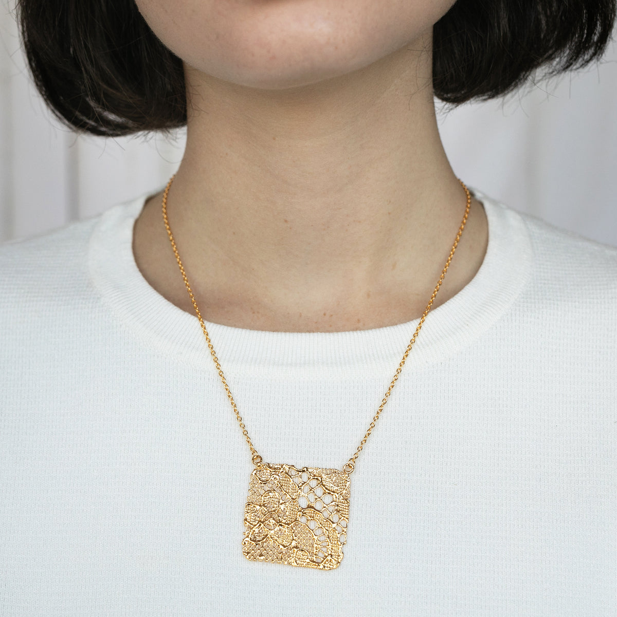 Intricate square pendant lace necklace in 24k gold worn by a model.