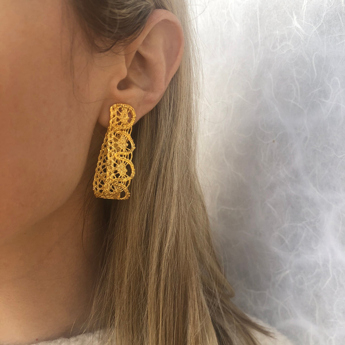 Model showing favorite earrings made from French 1920s lace forming a loop and solidified in 24k gold.